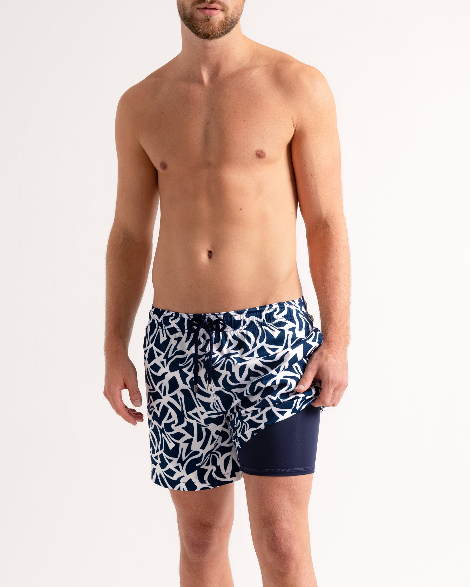 Man wearing navy swim shorts with white leaf pattern on a plain background