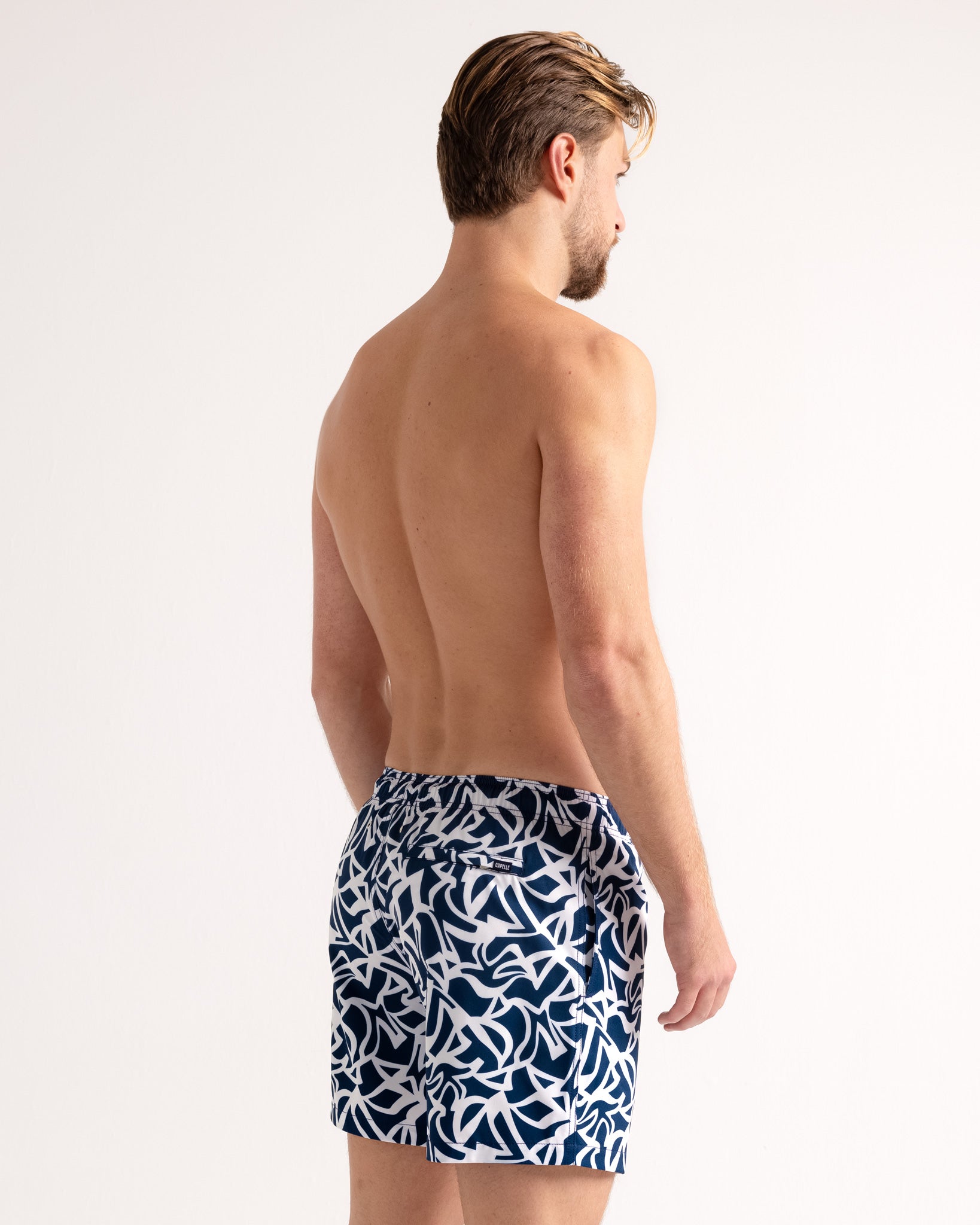 Man wearing navy and white patterned swim shorts on a white background