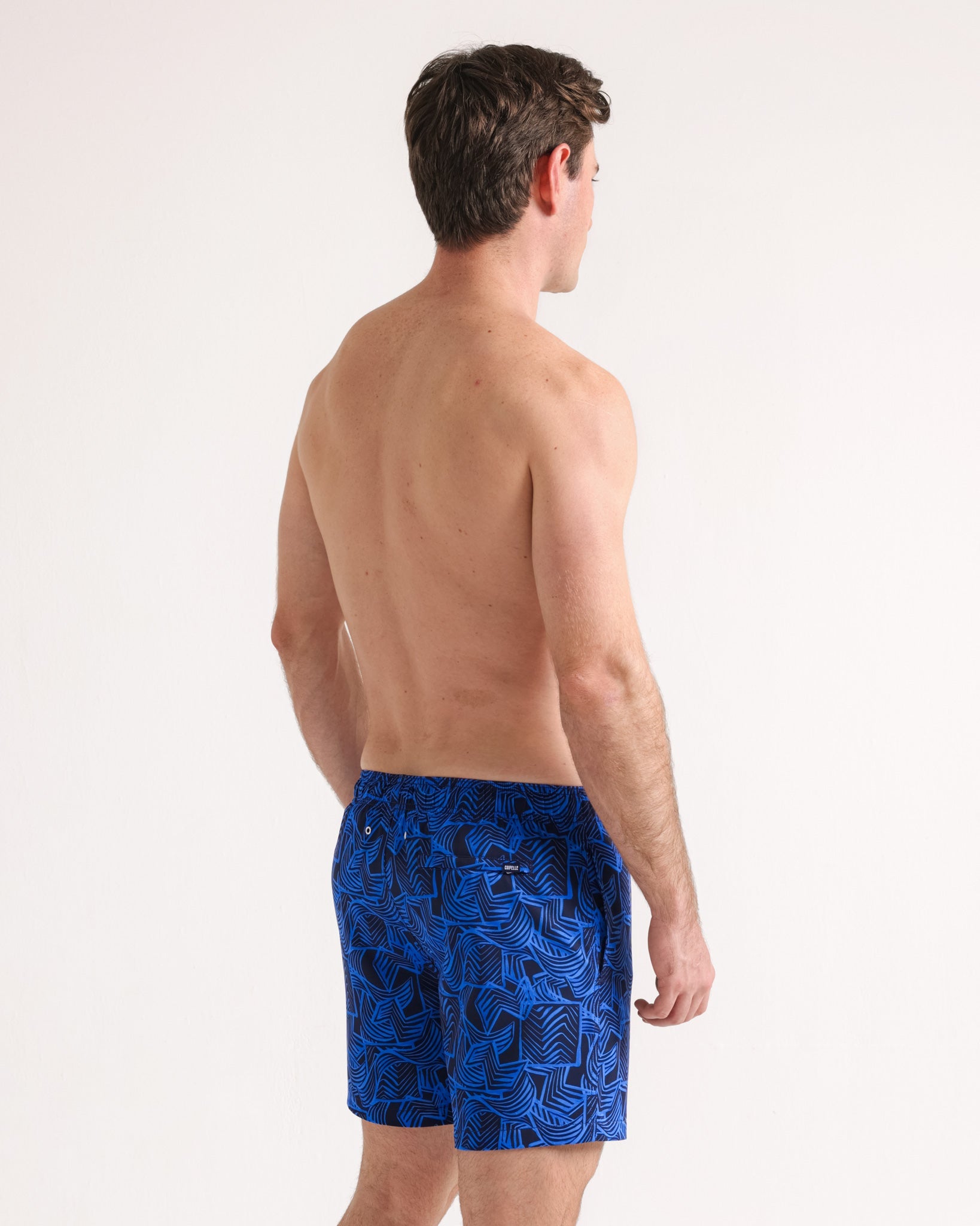 Man wearing blue swim shorts with a pattern on a white background