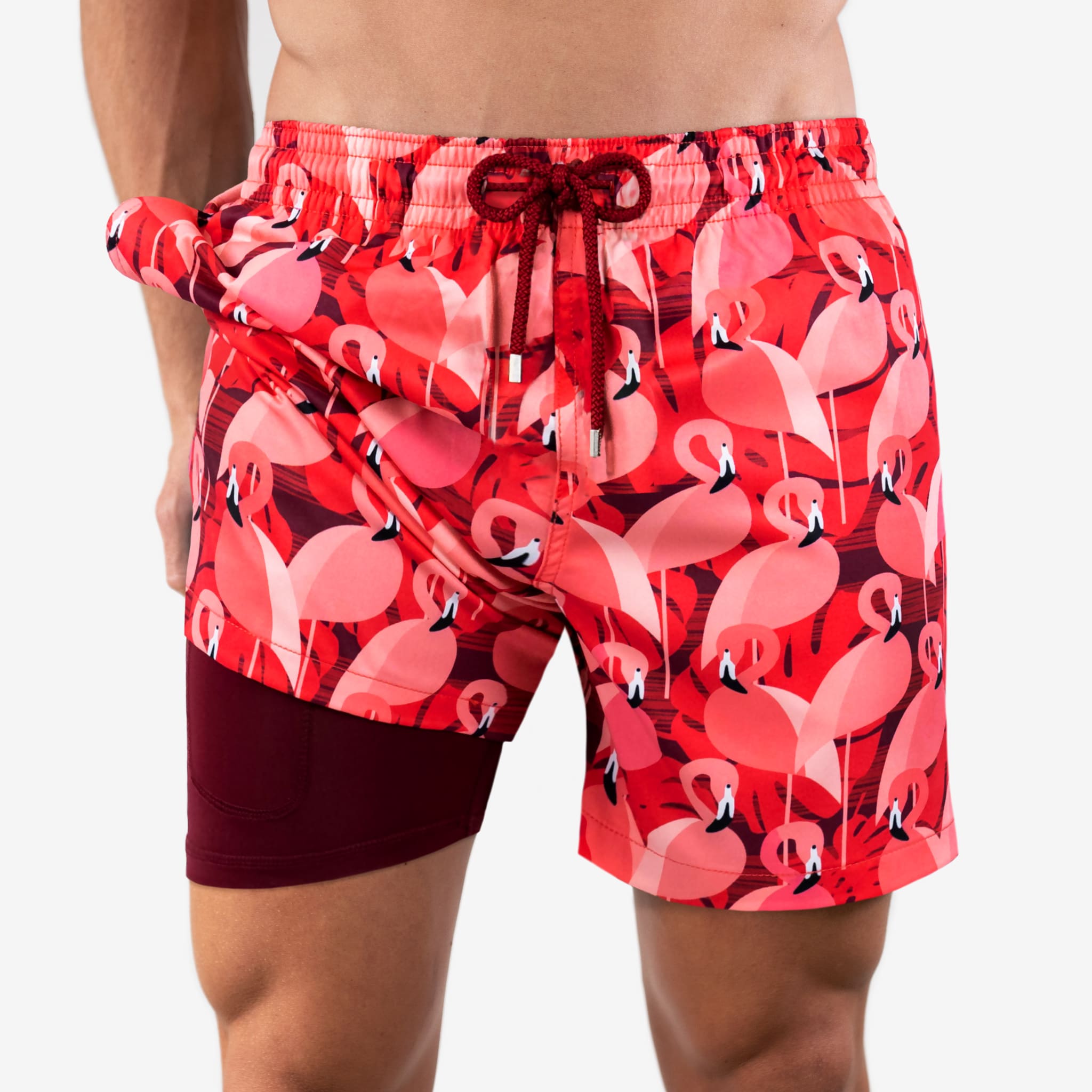 Red swim shorts with pink flamingo pattern worn by a person on a white background