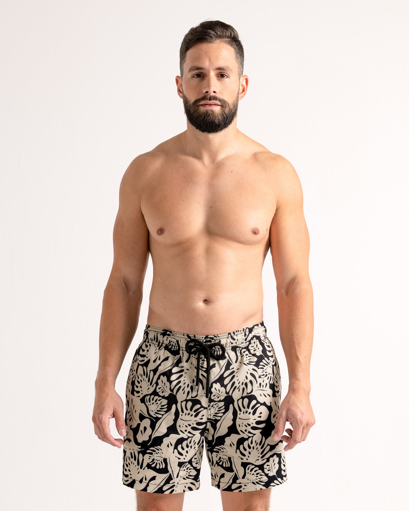 Man wearing black and white patterned swim shorts on a white background