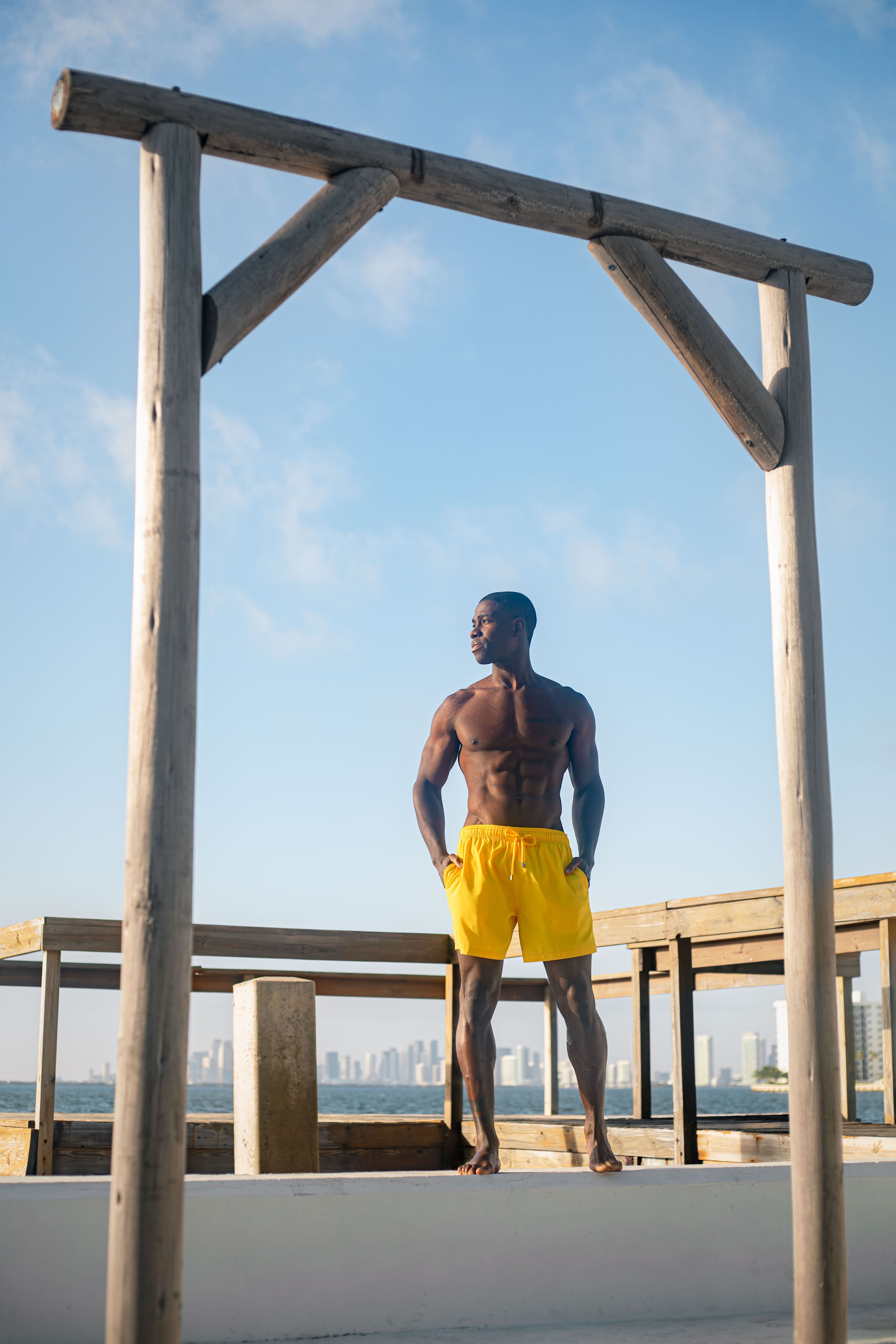 Man in yellow shorts standing on a wooden platform with a city skyline in the background