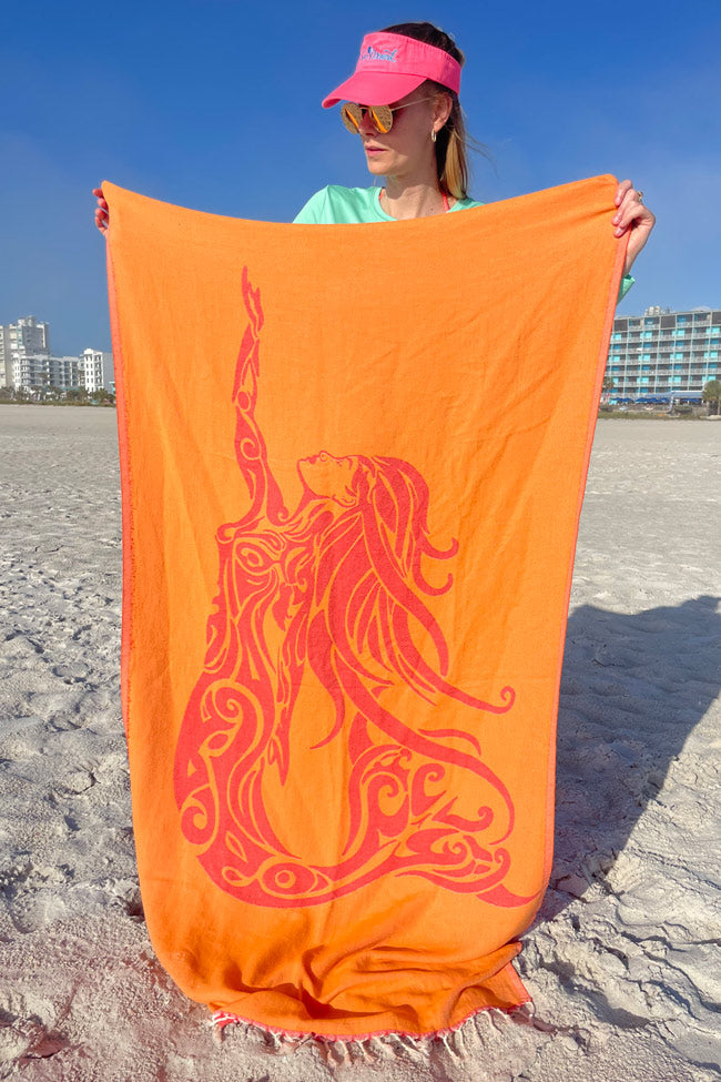 Person holding an orange towel with a red design on a beach