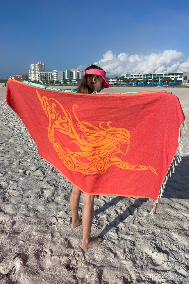 Person holding a red towel with orange dragon design on a beach