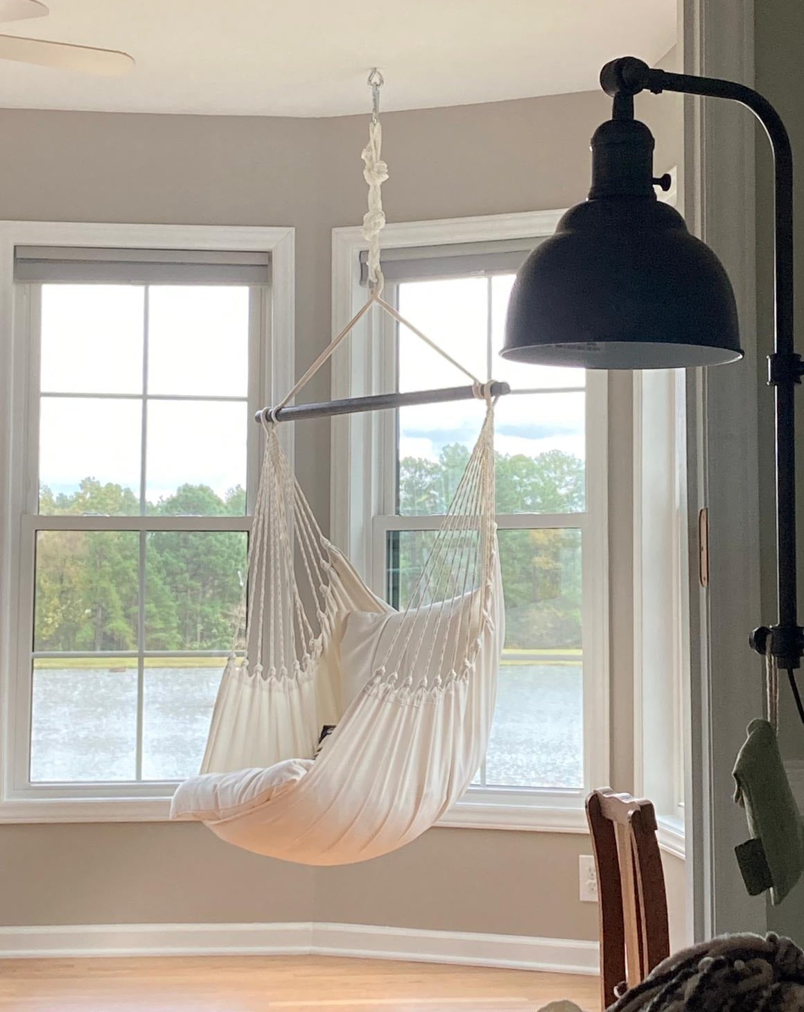 White hammock chair hanging in a room with large windows and a lamp.