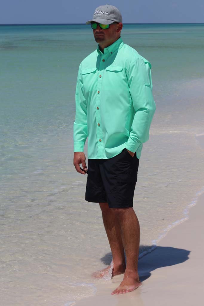 Man standing on a beach wearing a light green shirt and black shorts.