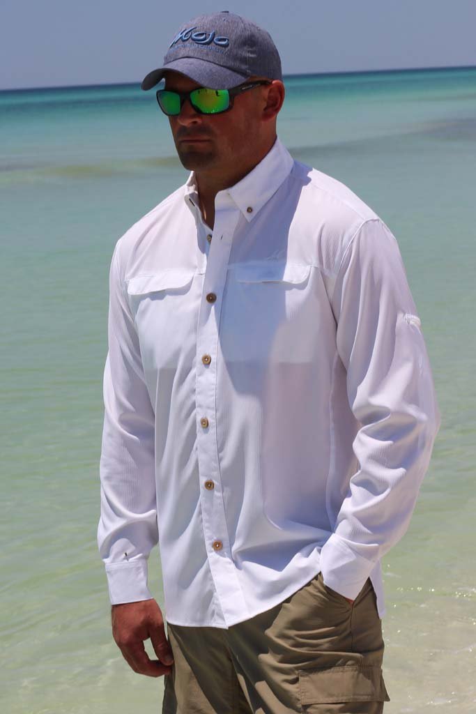 Man wearing a white shirt, khaki pants, and a cap with sunglasses on a beach.