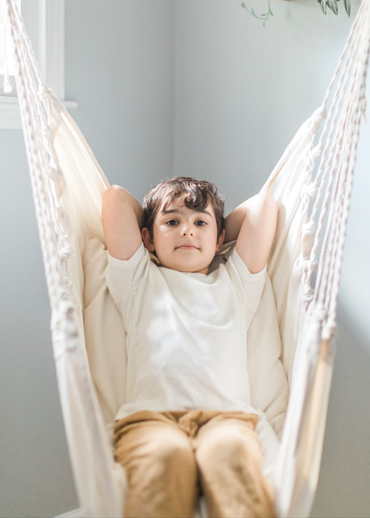 Child sitting in a white hammock against a light gray wall