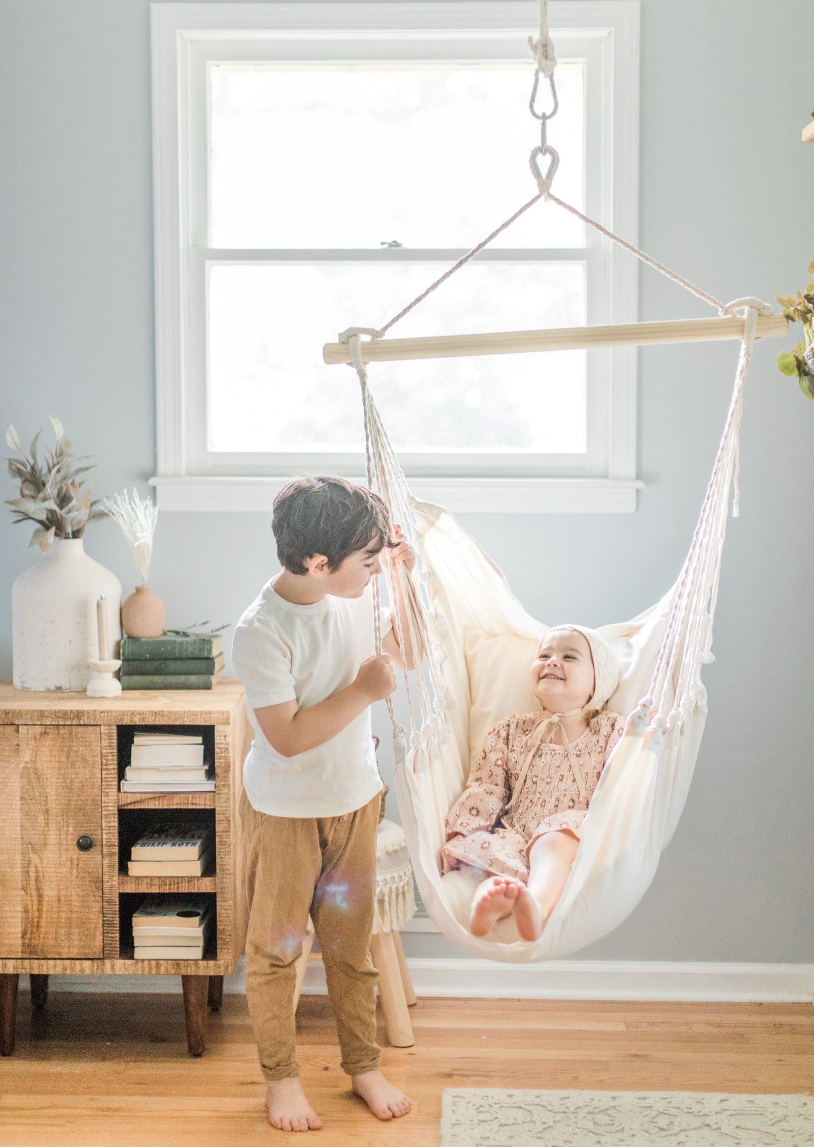 Two children in a room with a hanging hammock chair.