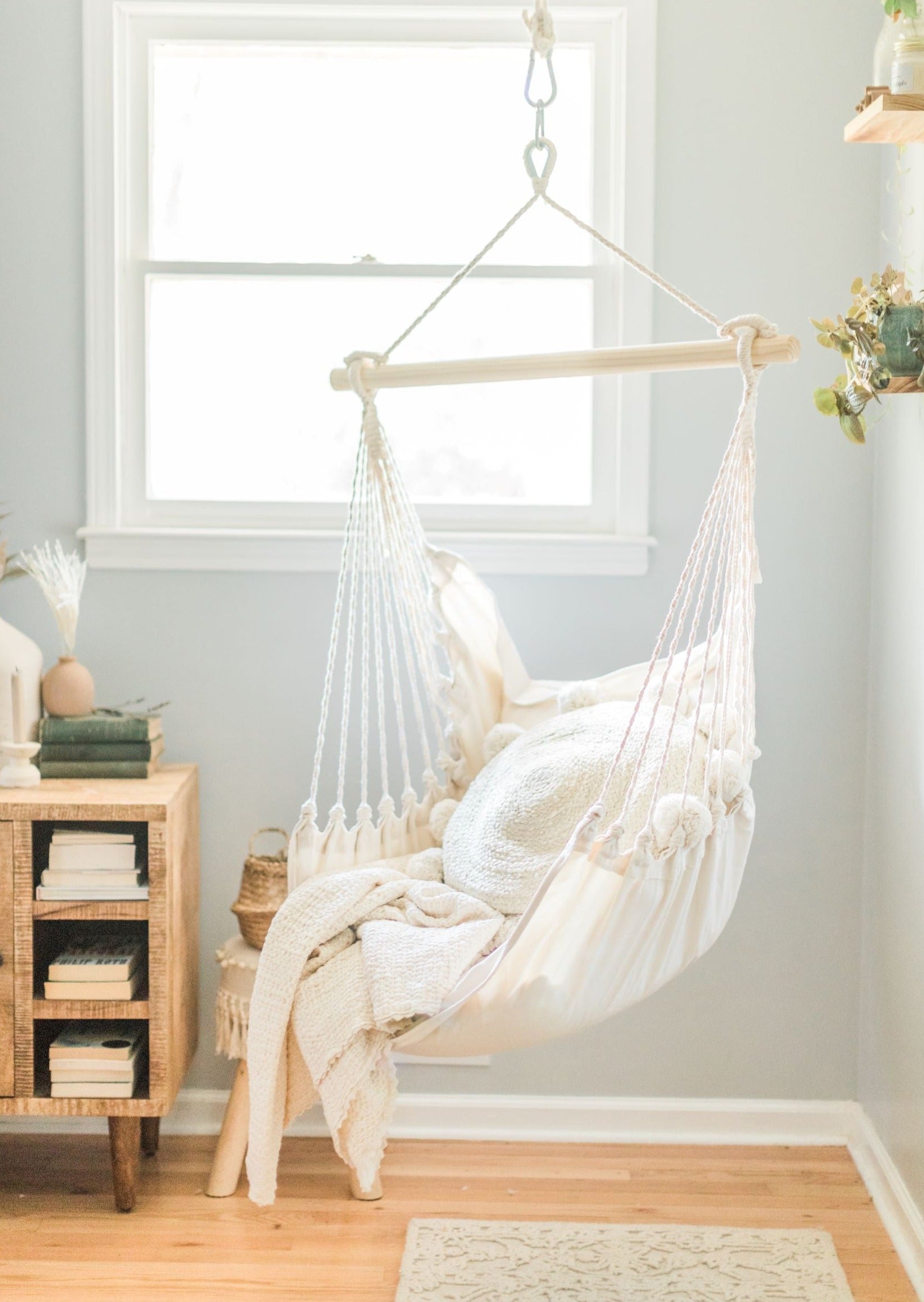 White hammock chair in a room with a wooden side table and window.
