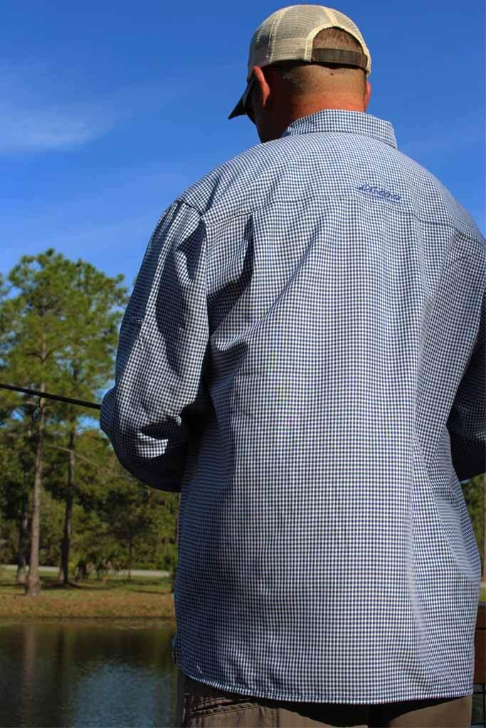 Man wearing a checkered shirt with a brand logo, standing by a body of water.