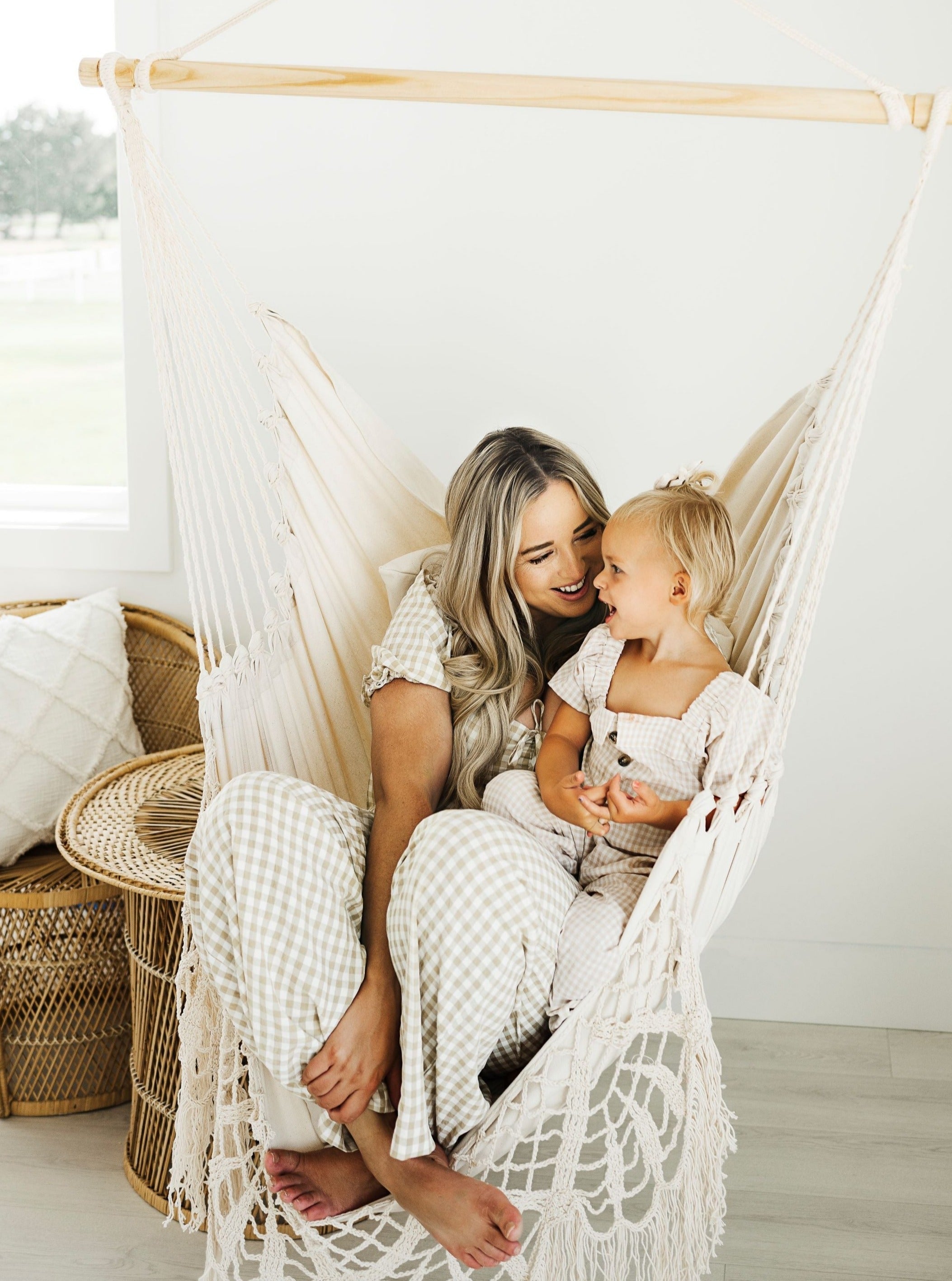 Woman and child sitting in a white macramé hammock indoors