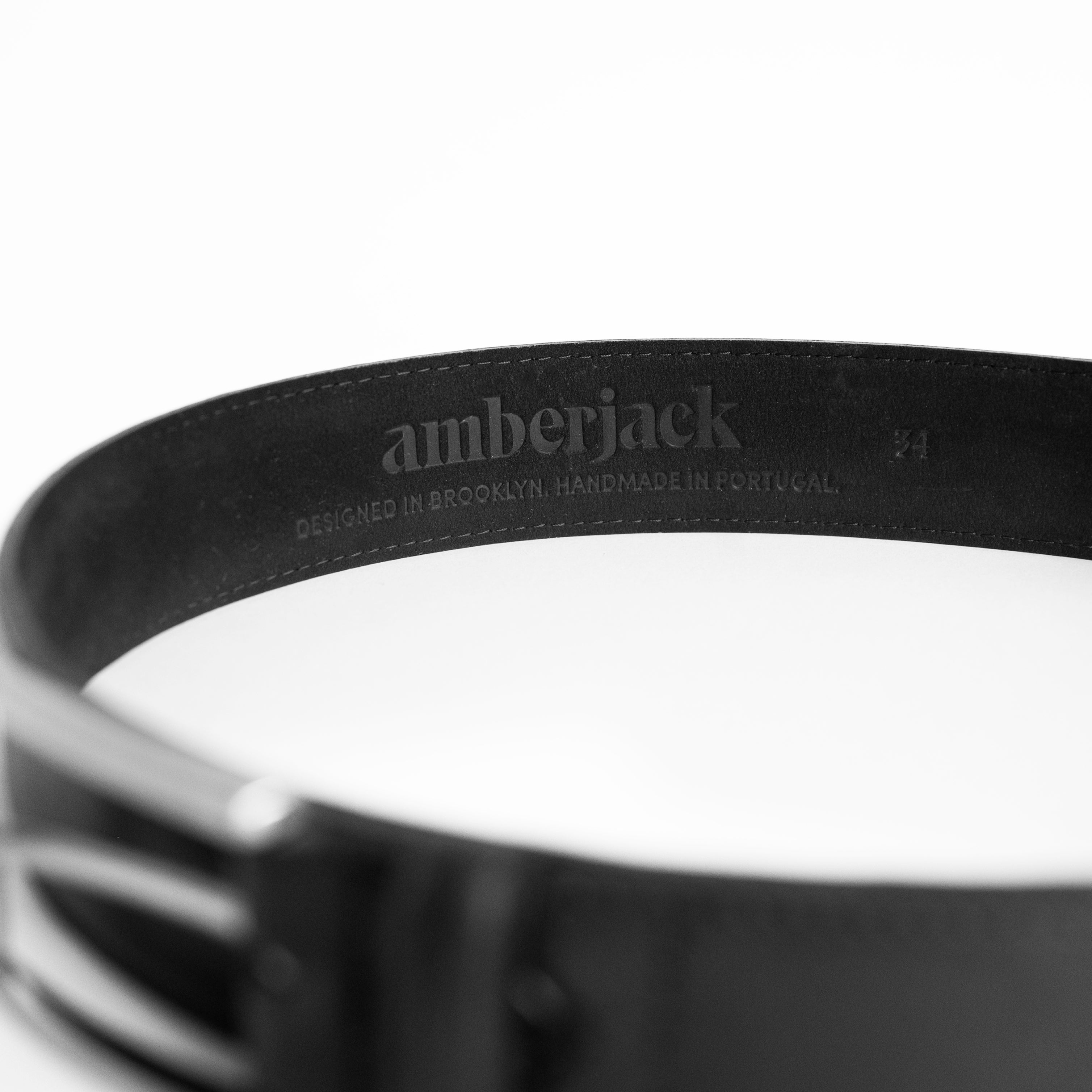 Close-up of a black belt with 'amberjack' branding on a white background