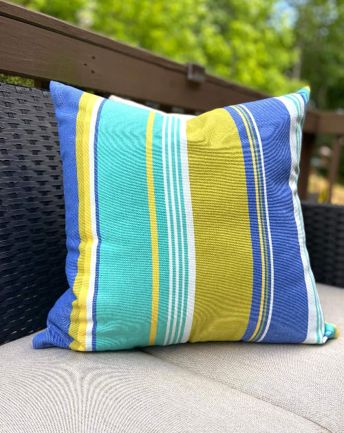 Striped pillow with blue, yellow, and green colors on a wicker chair outdoors.