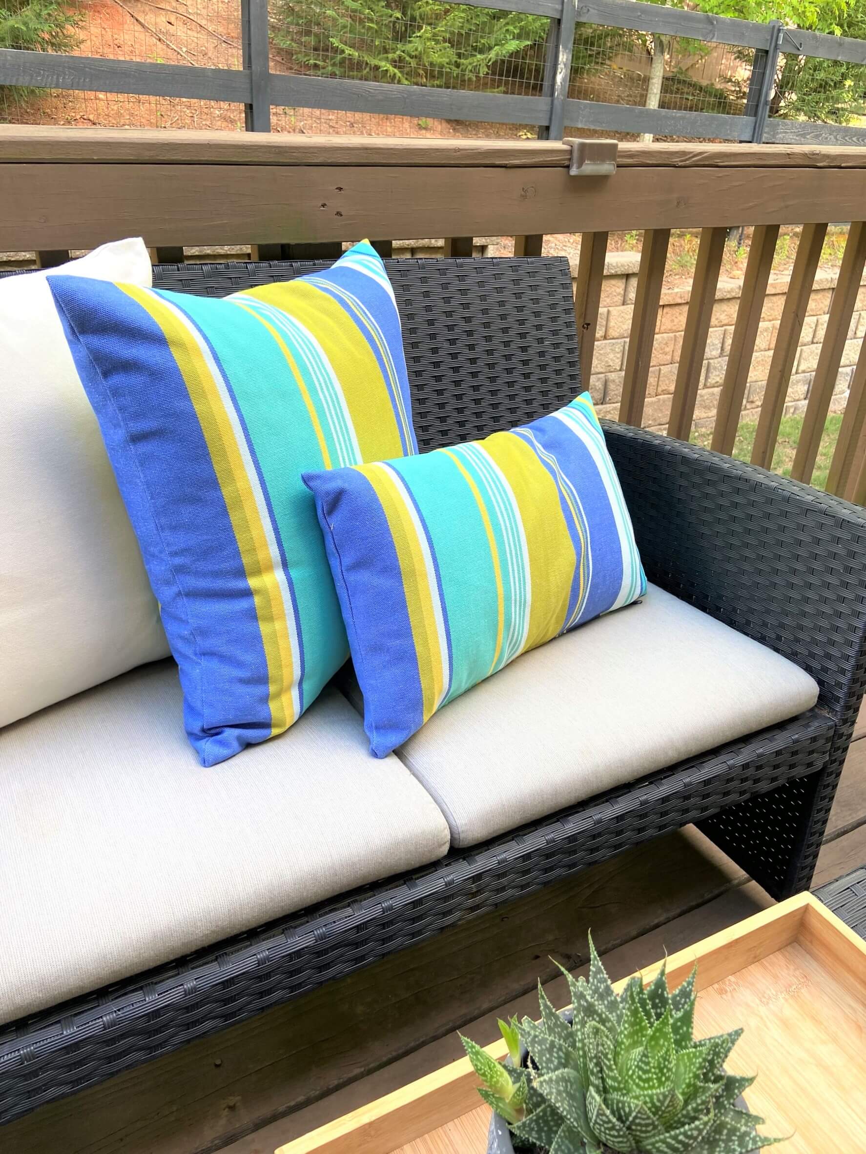 Outdoor wicker sofa with striped blue and yellow cushions on a wooden deck.