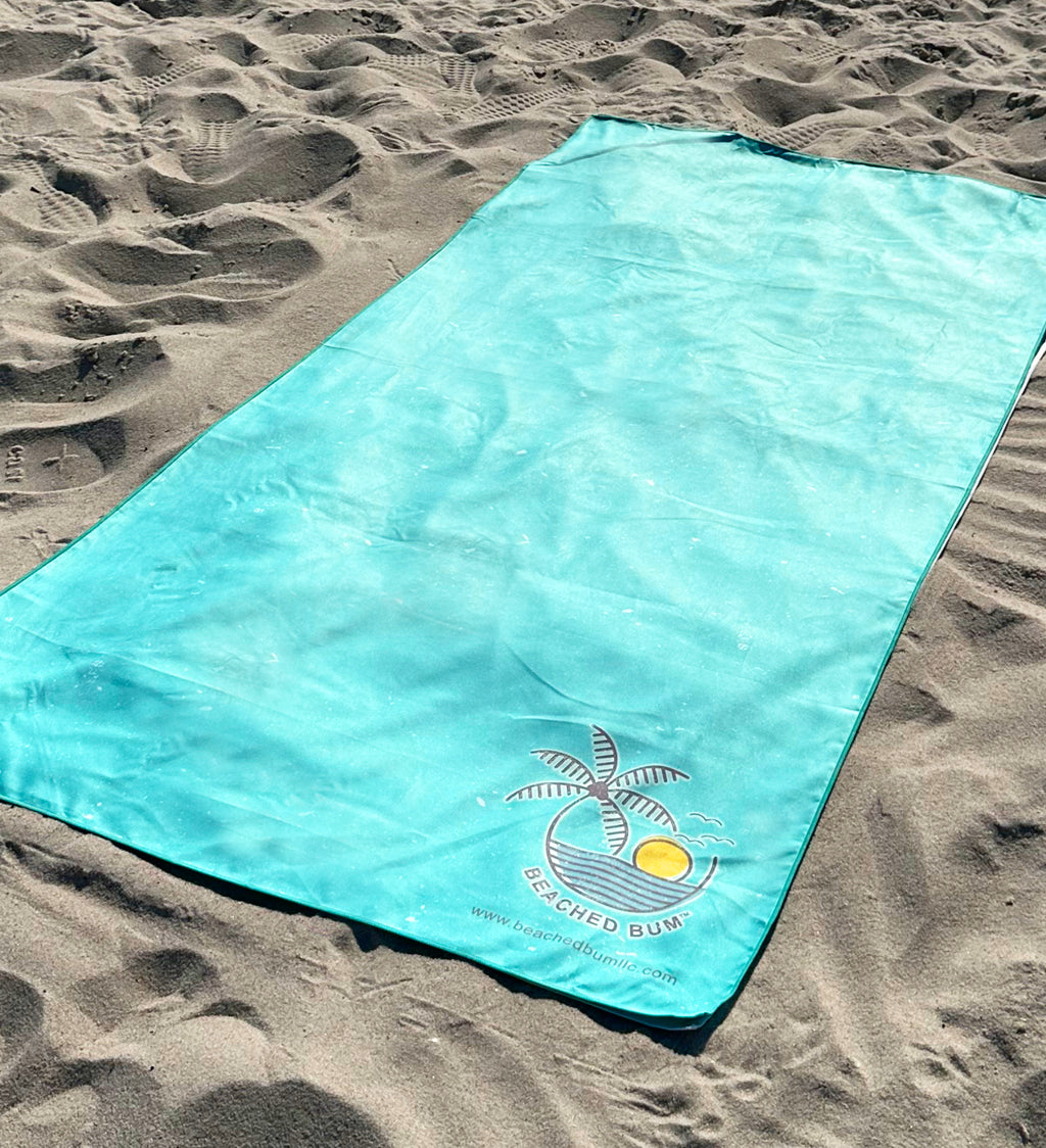 Turquoise beach towel with a palm tree design on sand