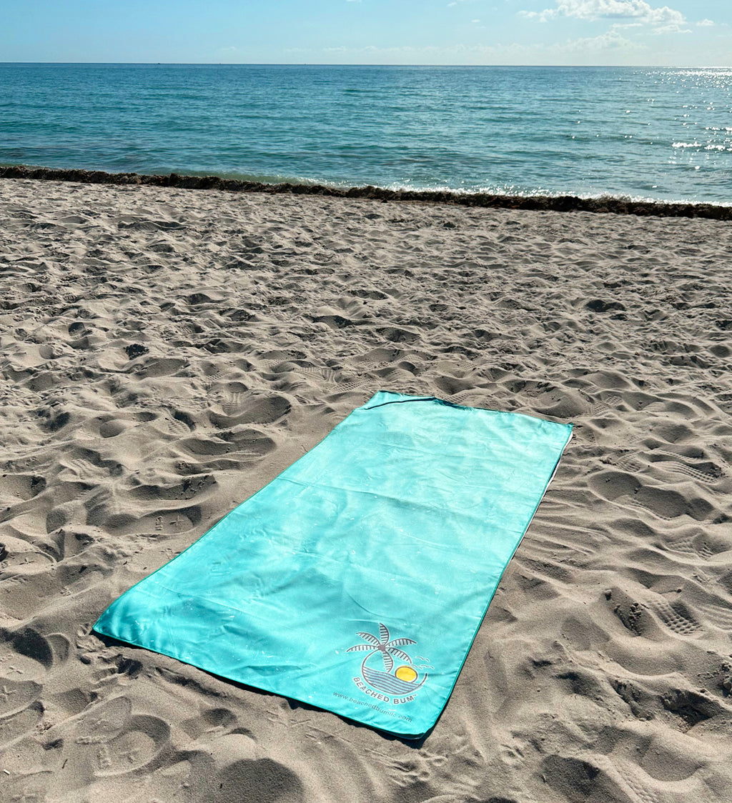 Turquoise beach towel with a logo on sand by the ocean