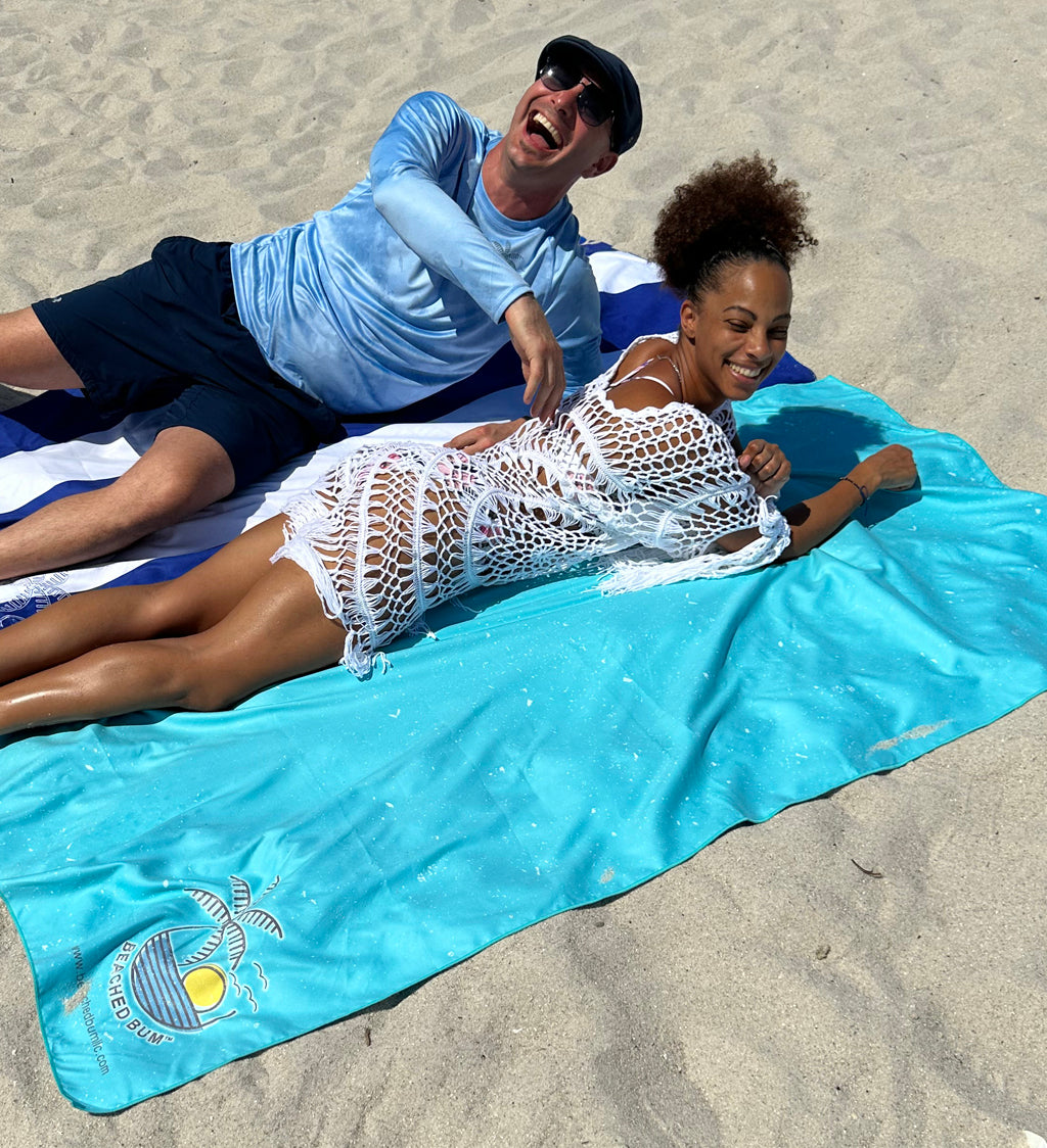 Two people lying on a blue towel at the beach