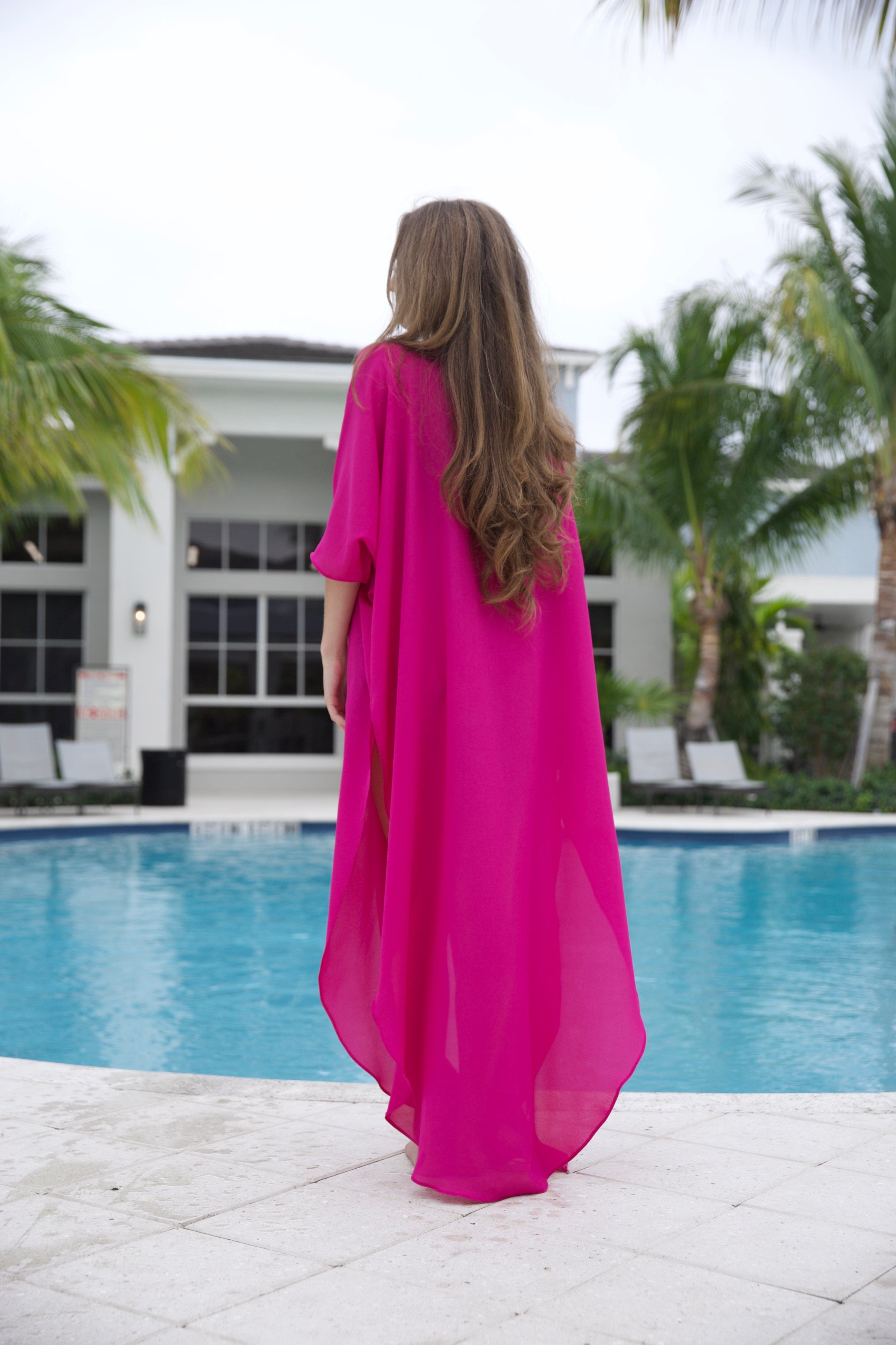 Woman in a pink dress standing by a pool with palm trees in the background