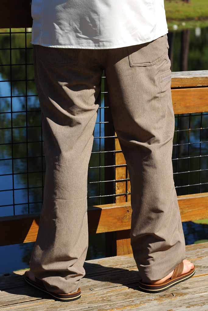 Person wearing brown pants standing on a wooden deck with a tiled wall and greenery in the background.