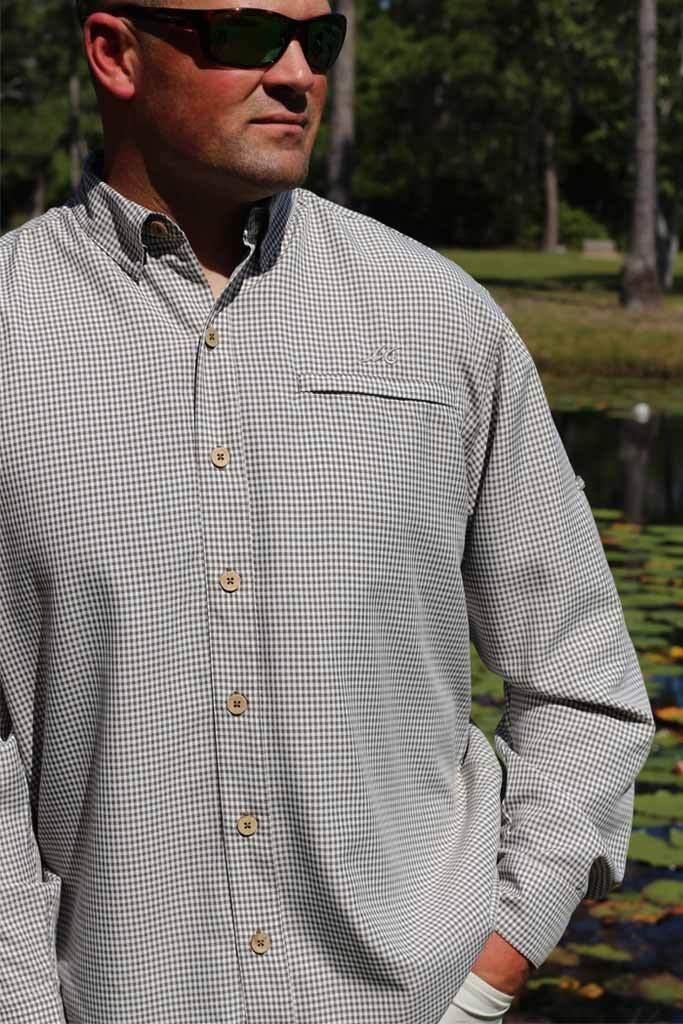 Man wearing a checkered shirt and sunglasses outdoors with trees and water in the background