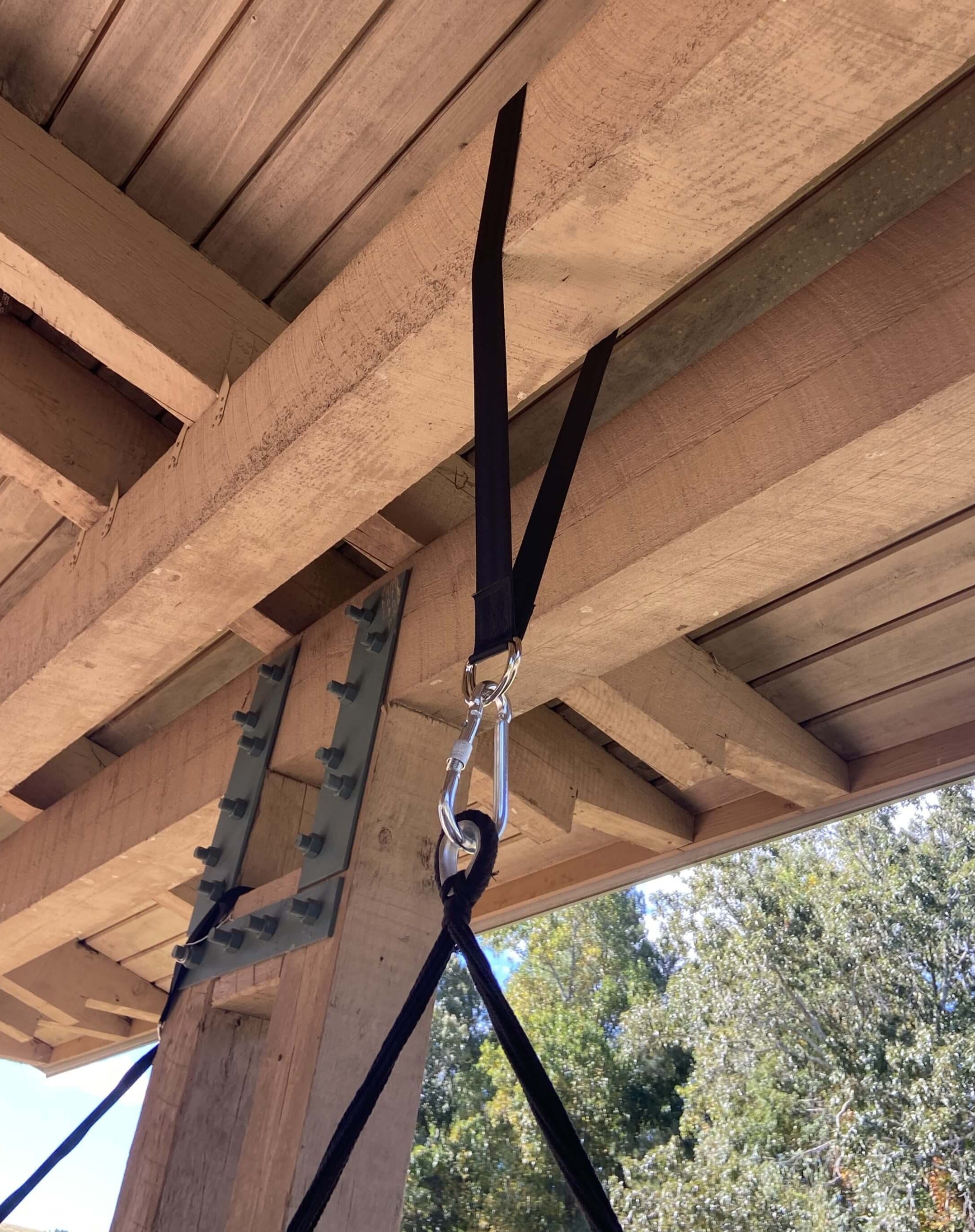 Hanging swing with straps attached to wooden beams with trees in the background