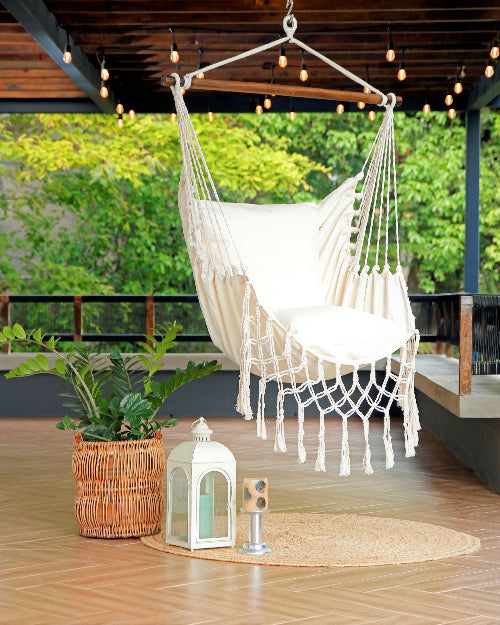 White macrame hammock chair on a wooden deck with plants and decor.