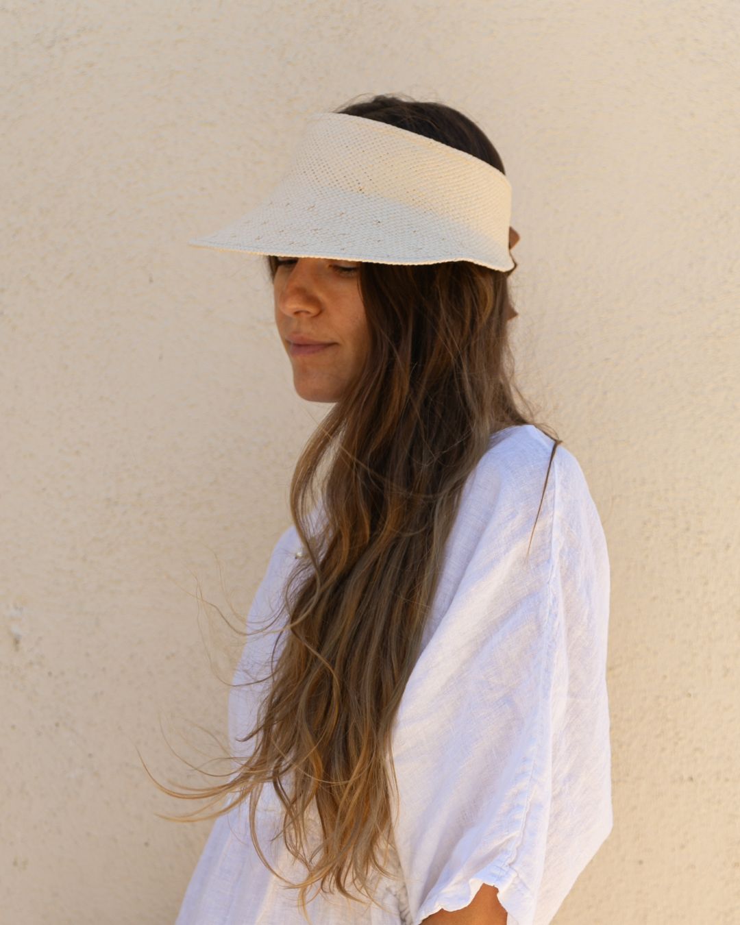Woman wearing a white visor and white top against a beige wall
