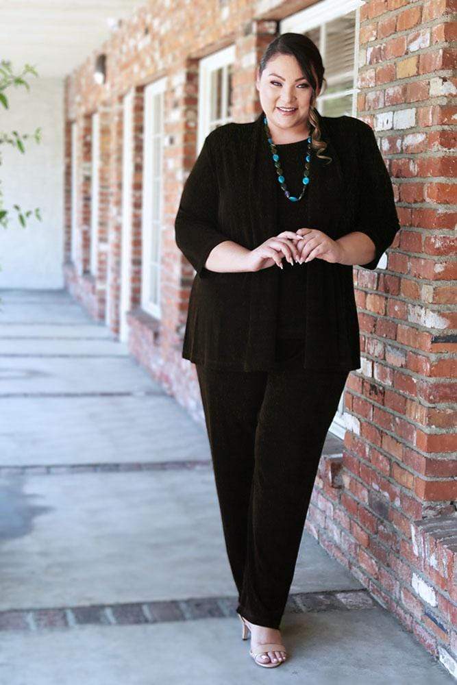 Woman in a black outfit standing against a brick wall.