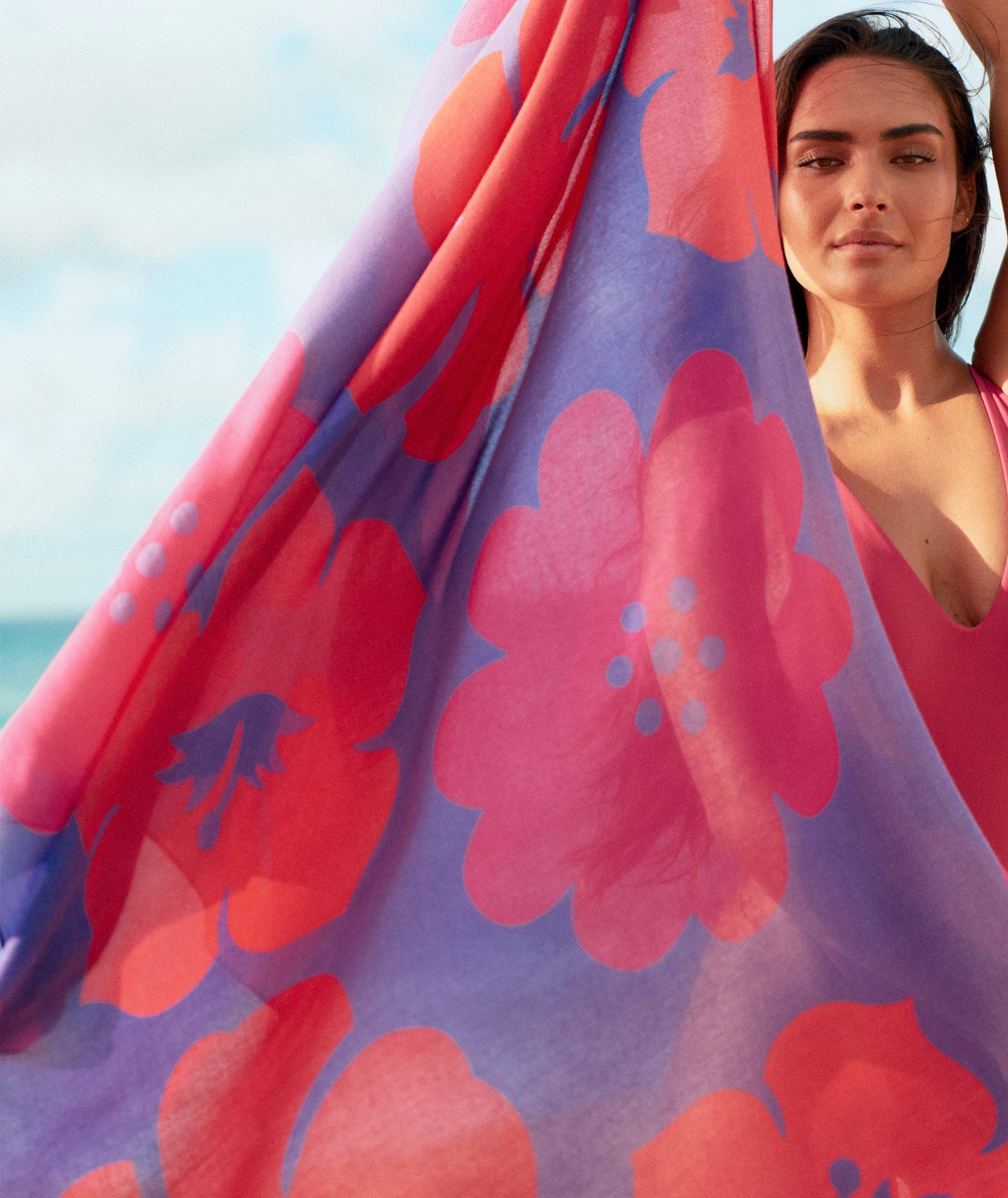 Woman holding a colorful floral towel with a beach in the background
