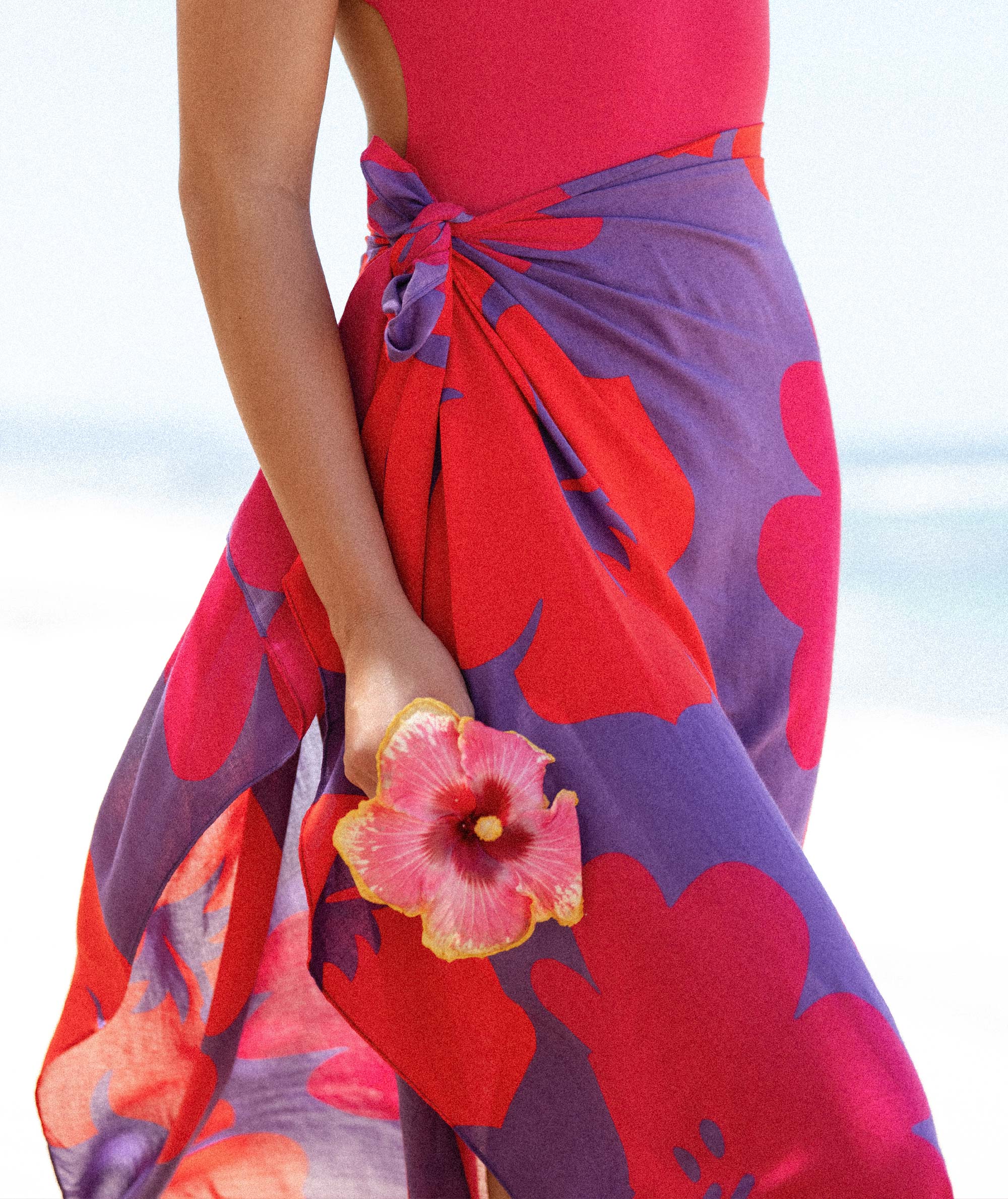 Person wearing a red and purple floral dress with a flower accessory against a light background