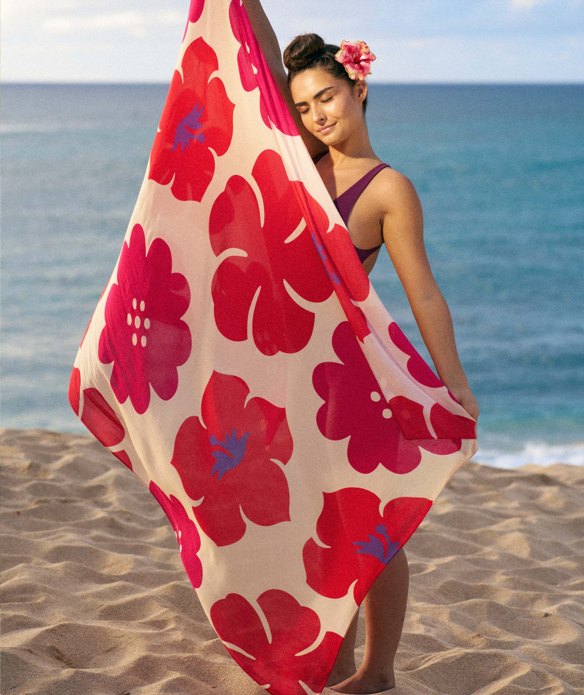 Woman holding a red floral towel on a beach