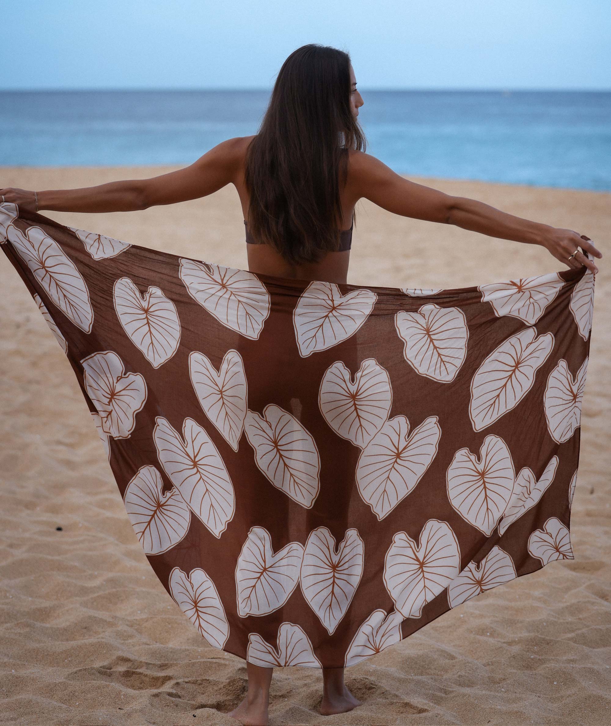 Woman on a beach with a brown and white leaf-patterned sarong