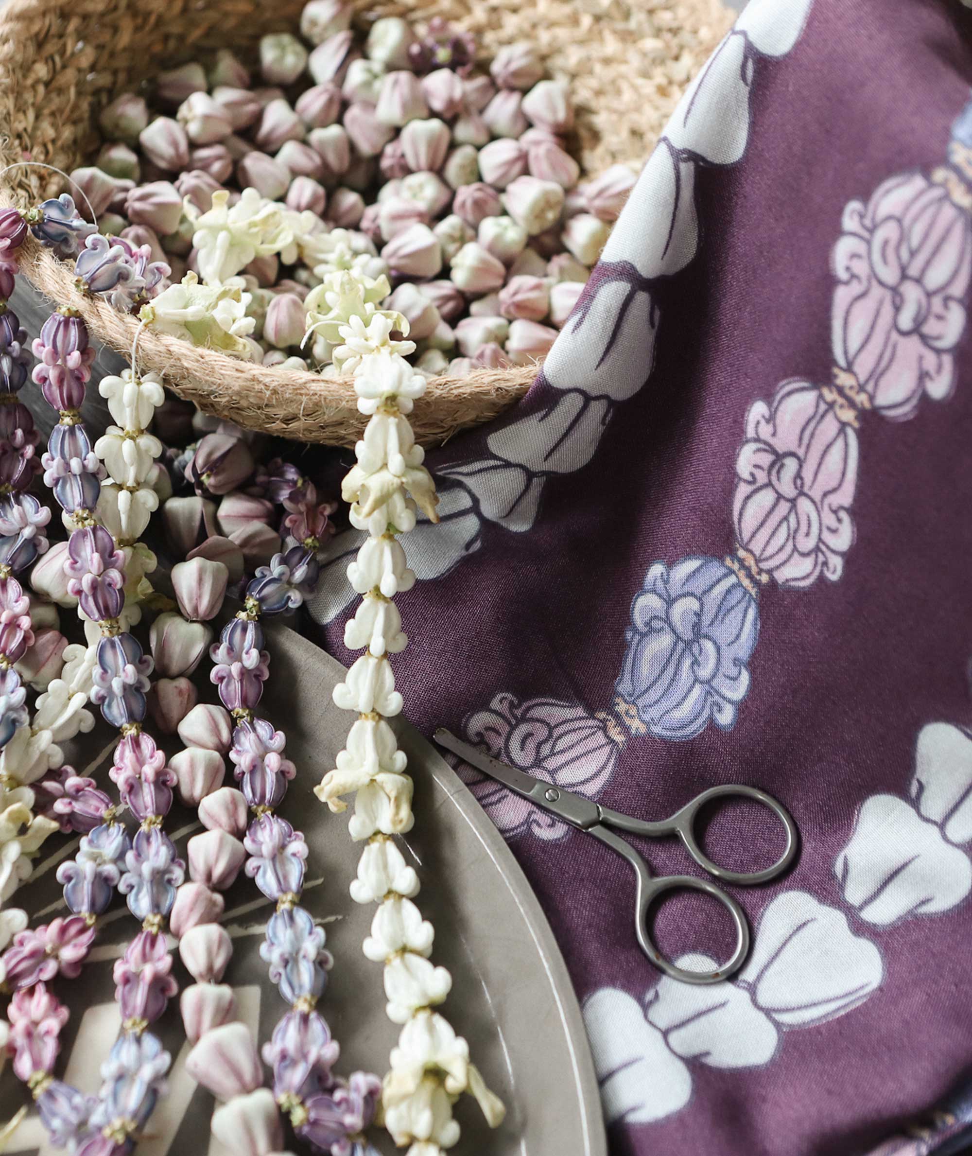 Necklace-making materials including beads, scissors, and a patterned cloth on a textured surface.