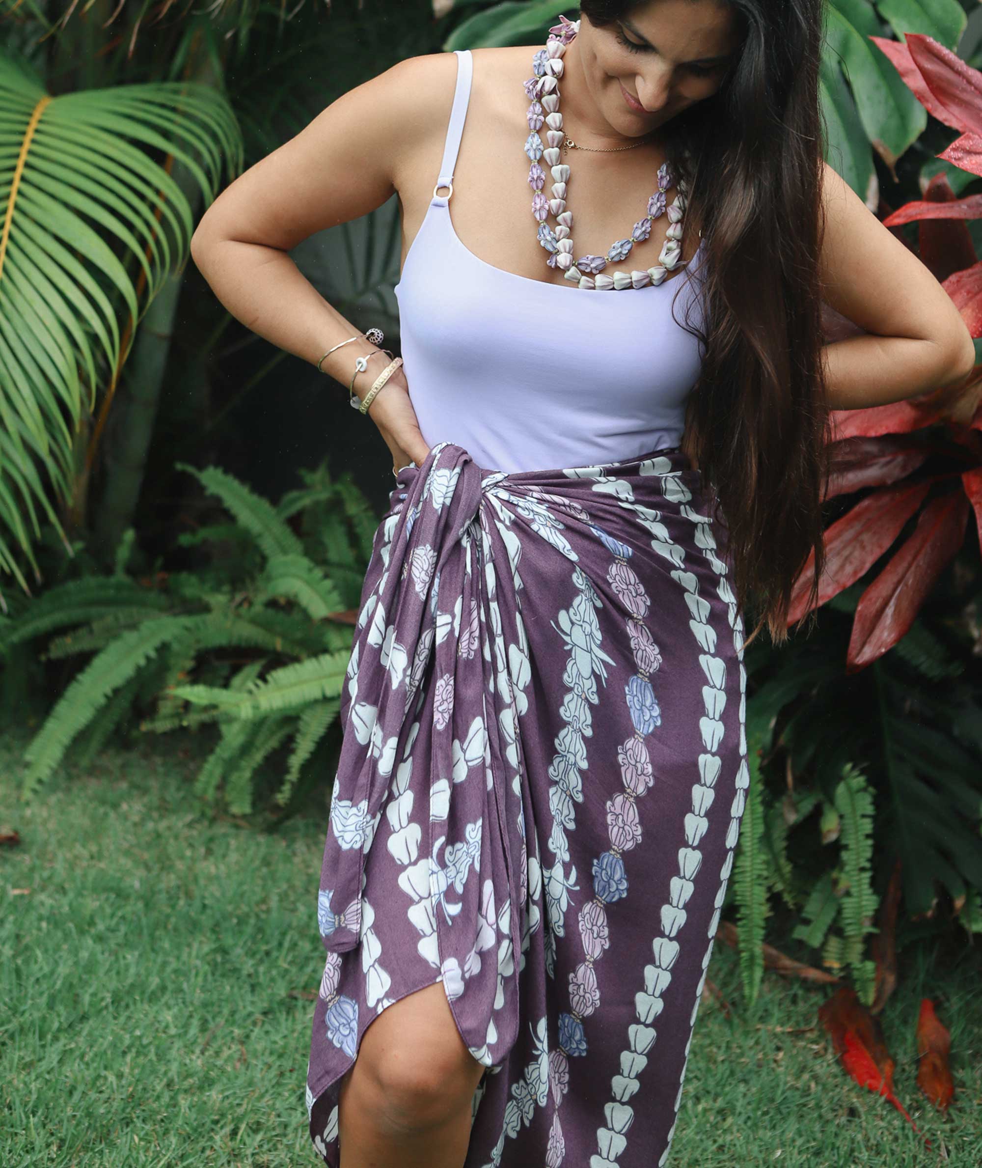 Woman wearing a white top and purple floral sarong in a garden setting