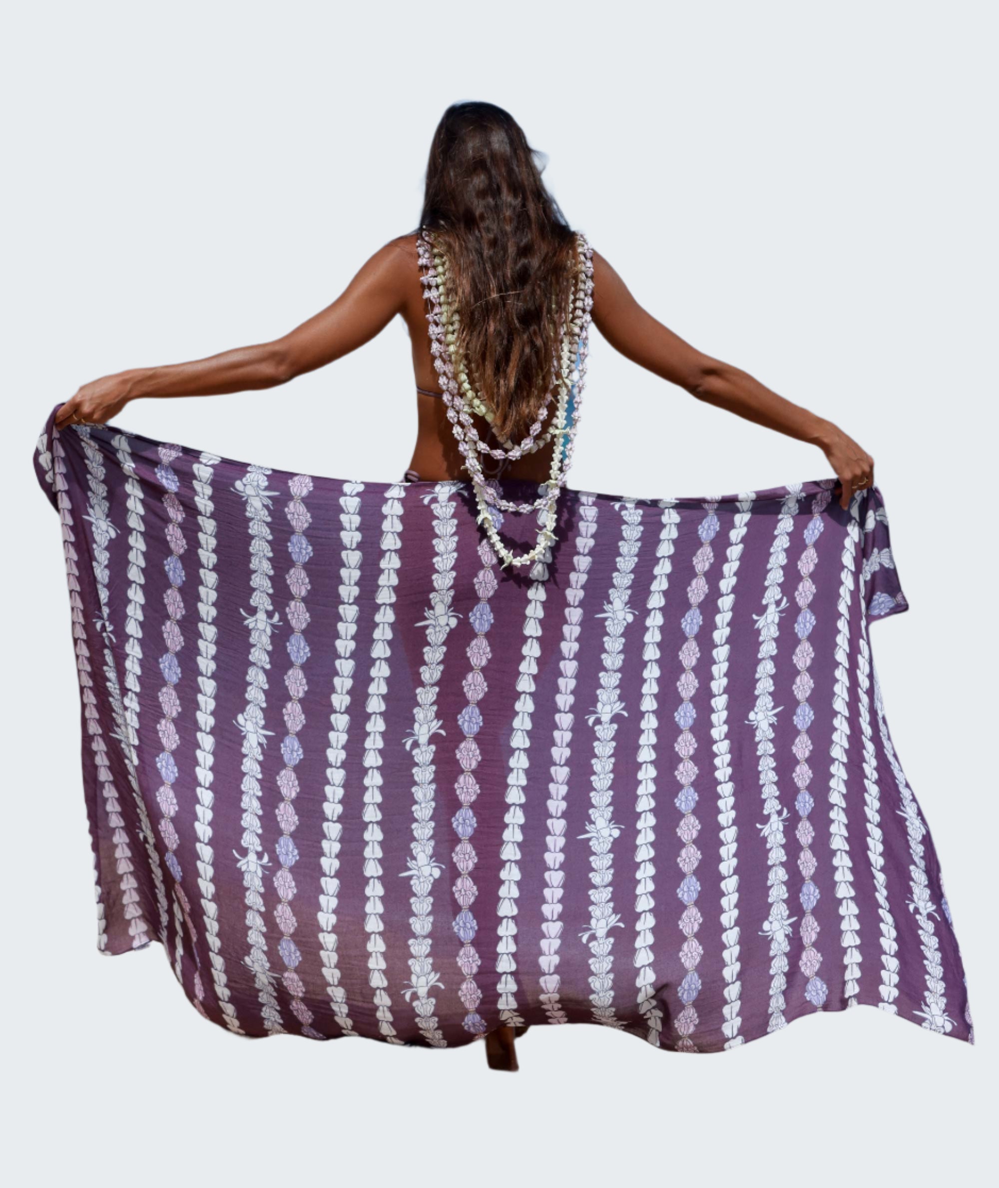 Person holding a purple and white patterned towel on a beach with blue water and sky.