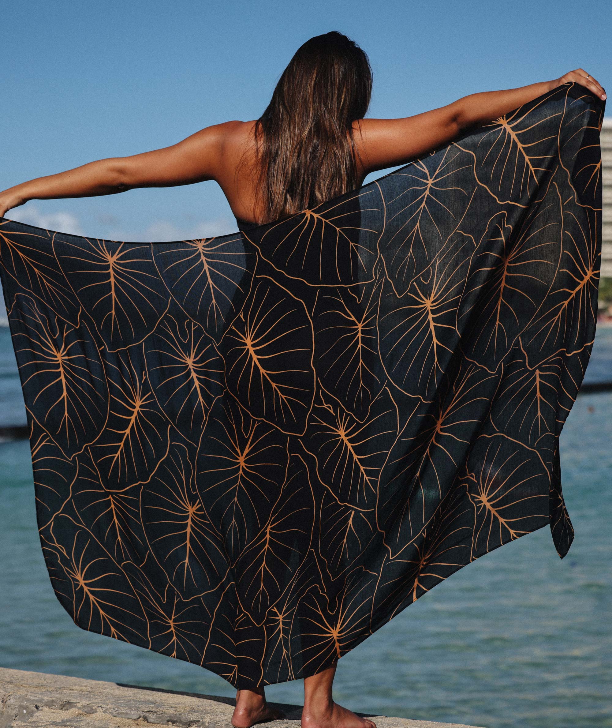 Person holding a black fabric with gold leaf pattern by the water