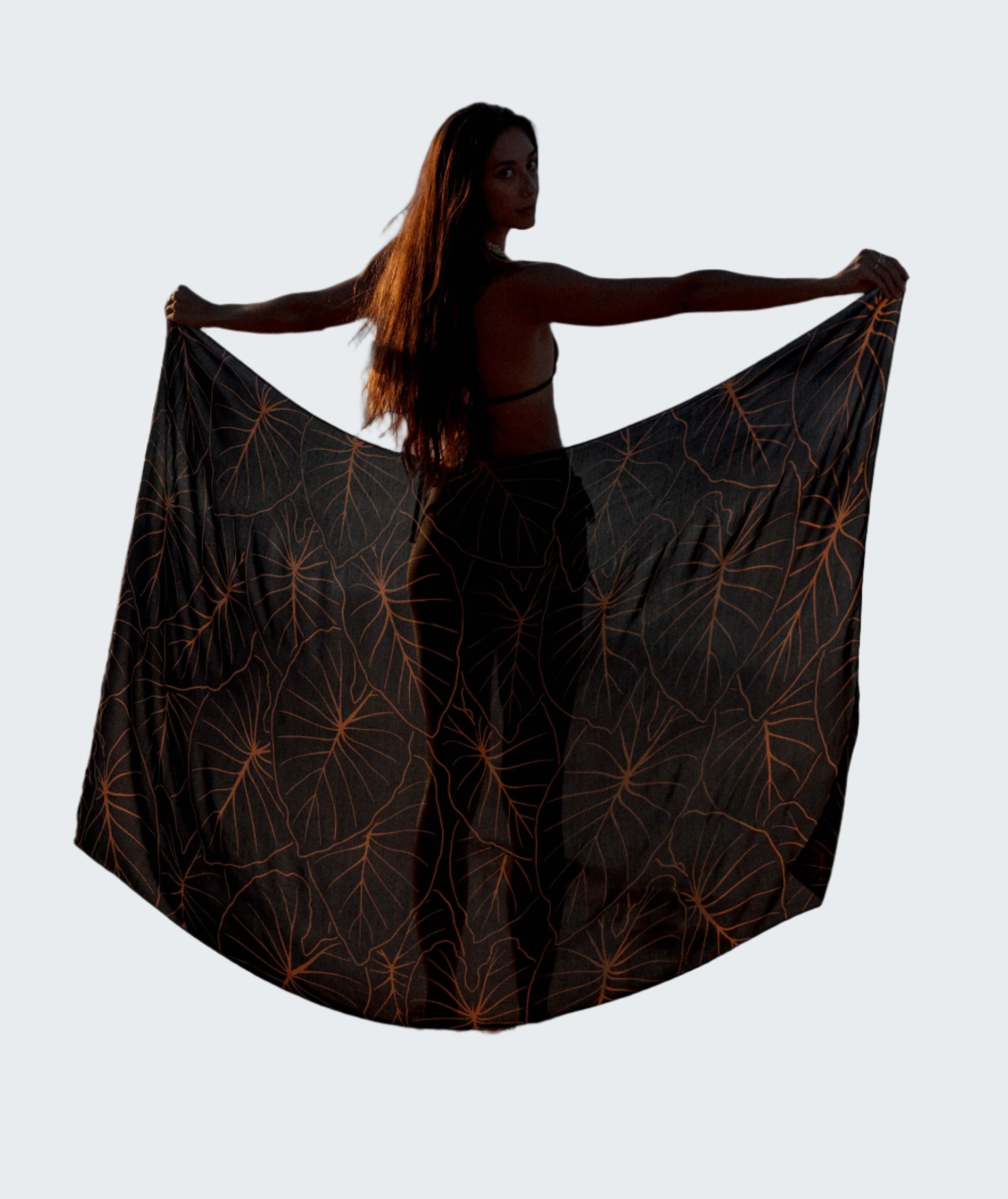 Woman holding a black patterned fabric on a beach with ocean waves in the background