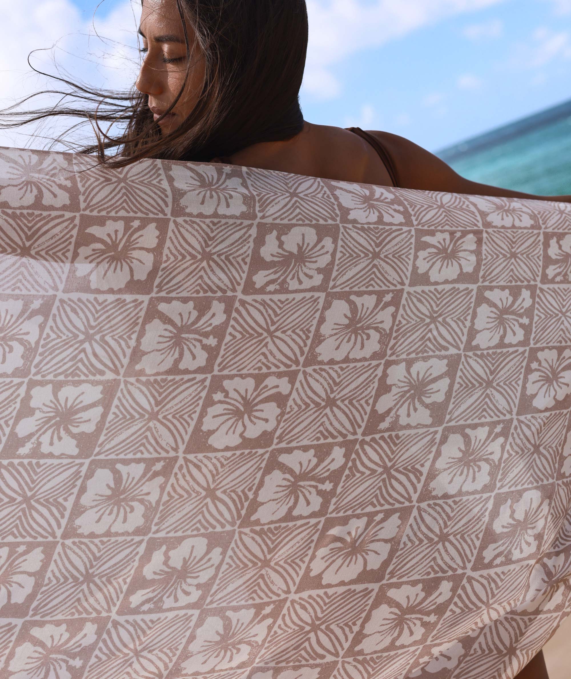 Person holding a patterned towel with a beach in the background