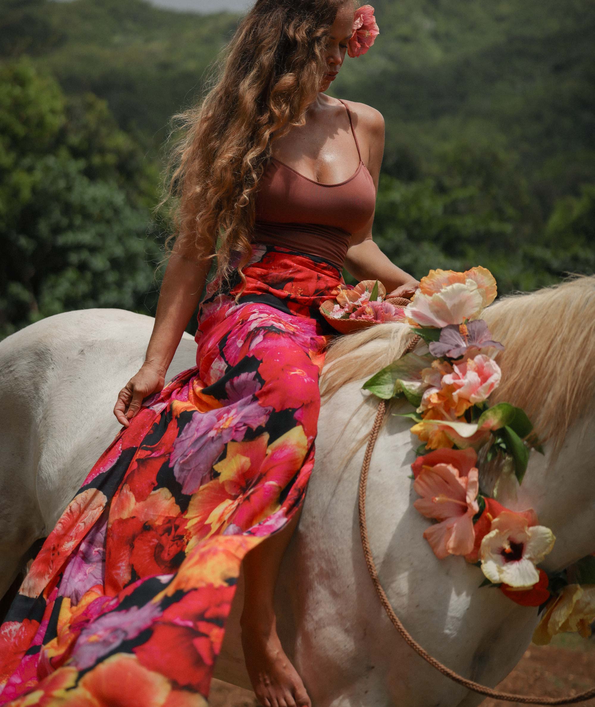 Woman in a colorful dress sitting on a horse with a floral arrangement in a natural setting