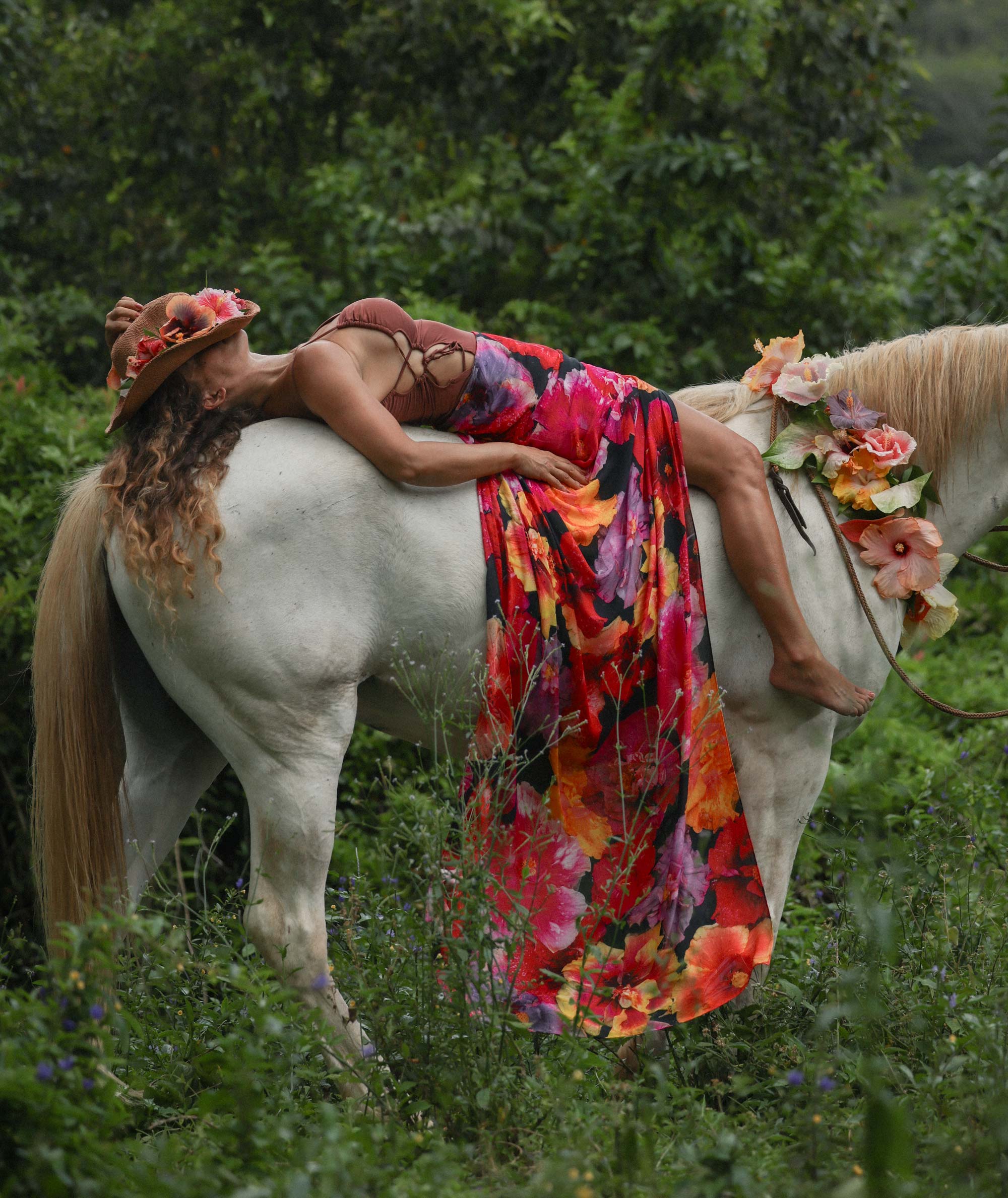 Person in a colorful dress and hat sitting on a white horse in a forest setting
