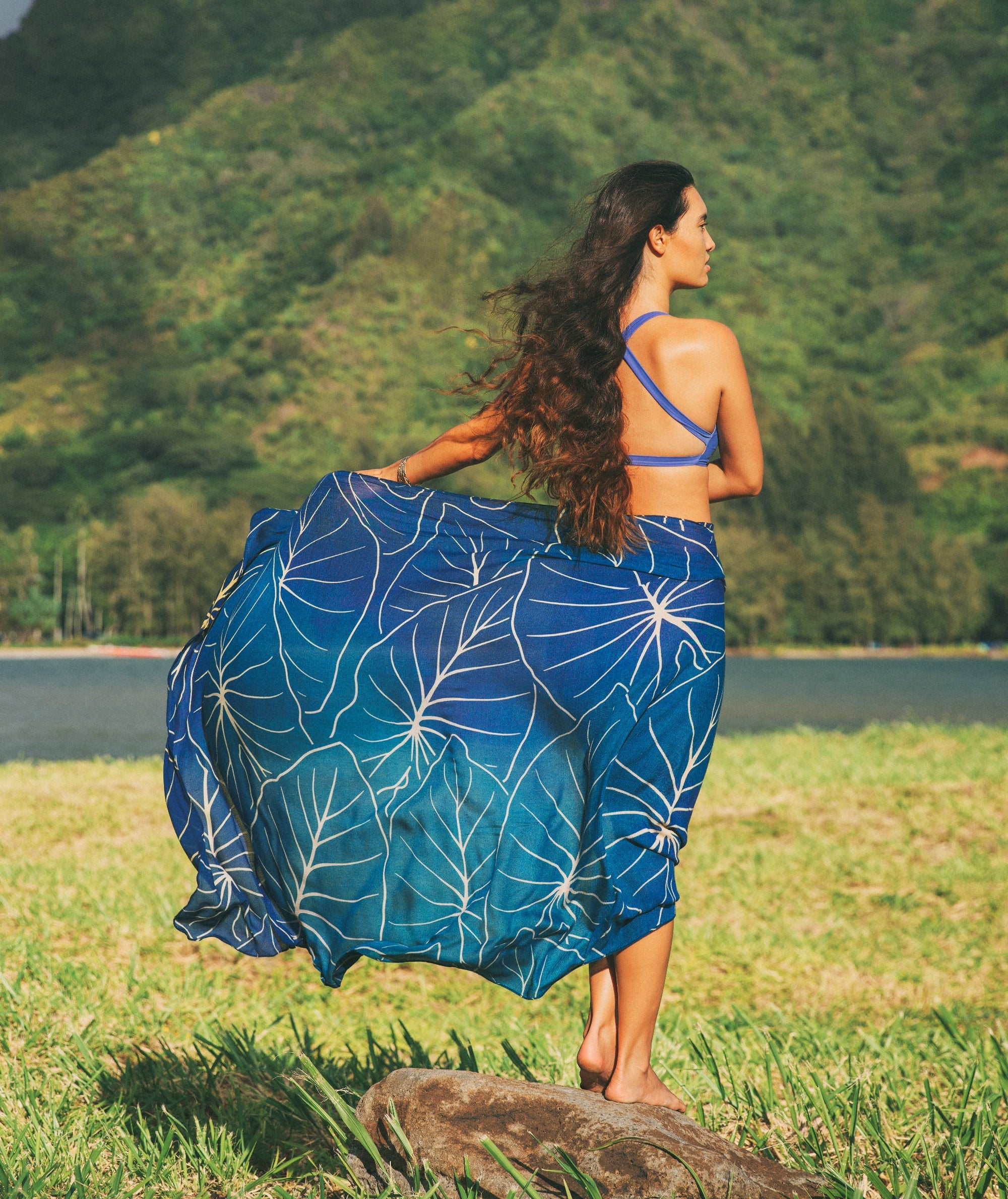 Woman in a blue bikini with a matching sarong standing on grass with mountains in the background