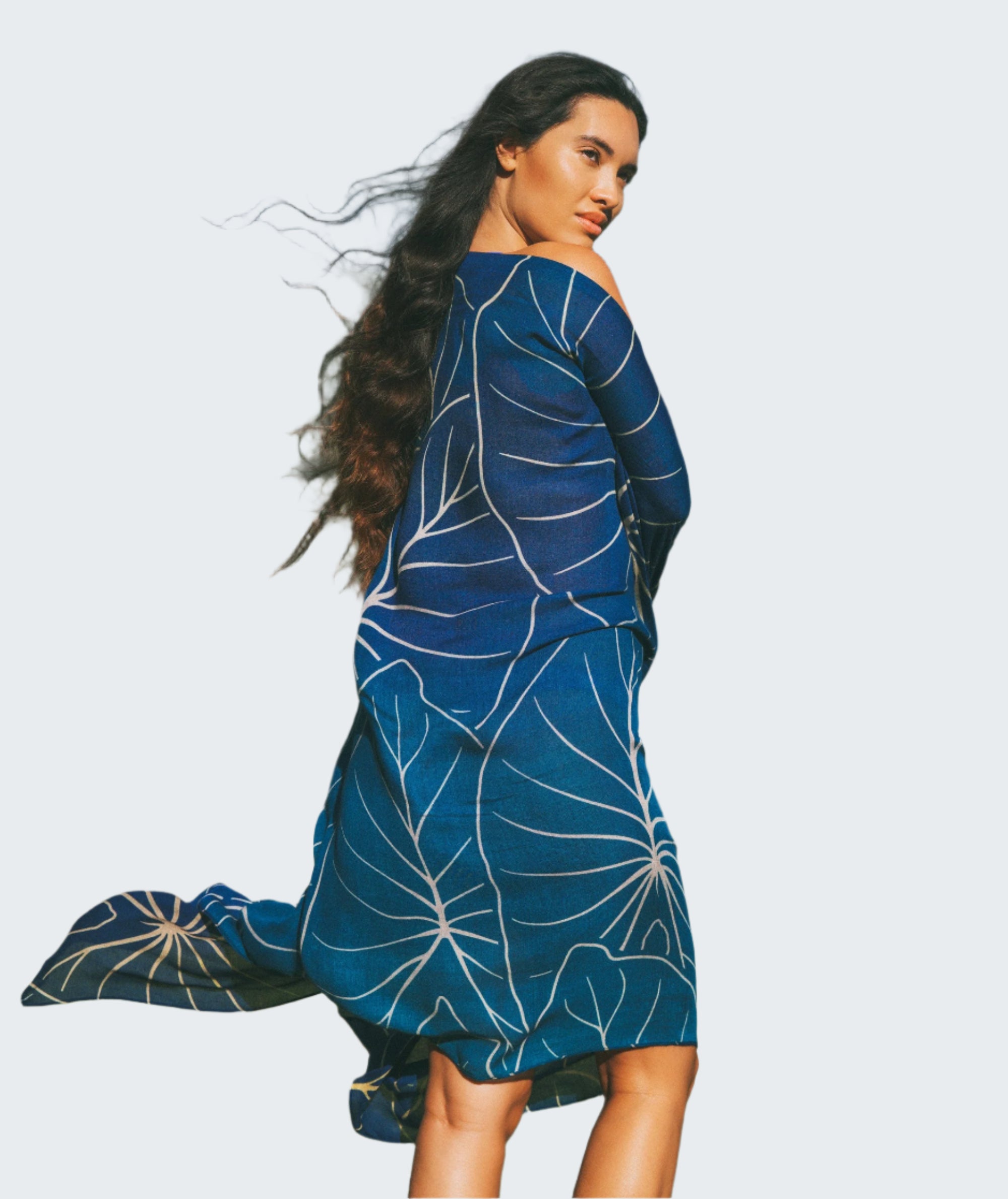 Woman wearing a blue dress with white patterns standing in a grassy area with mountains in the background