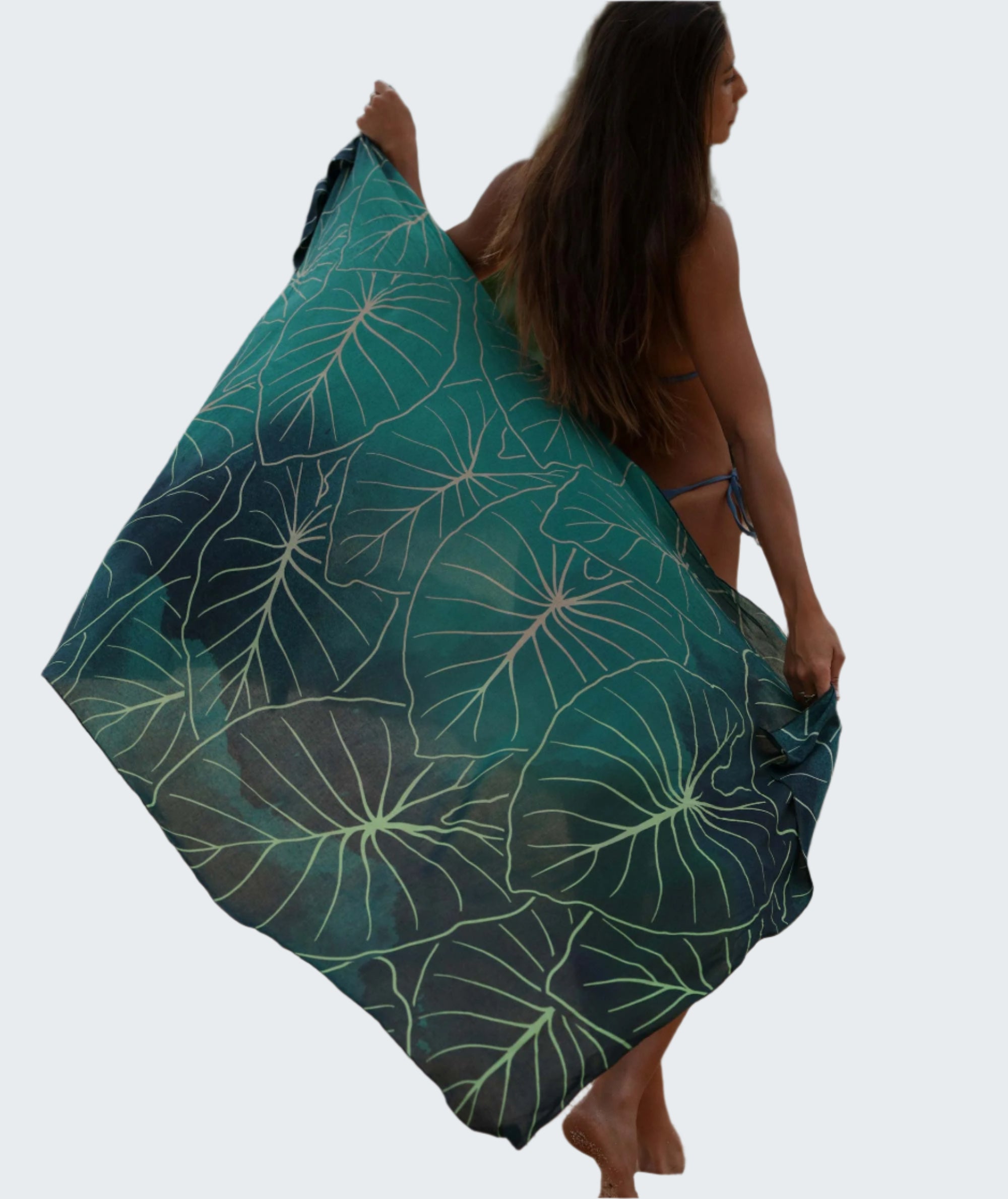 Woman holding a green leaf-patterned towel on a sandy beach.