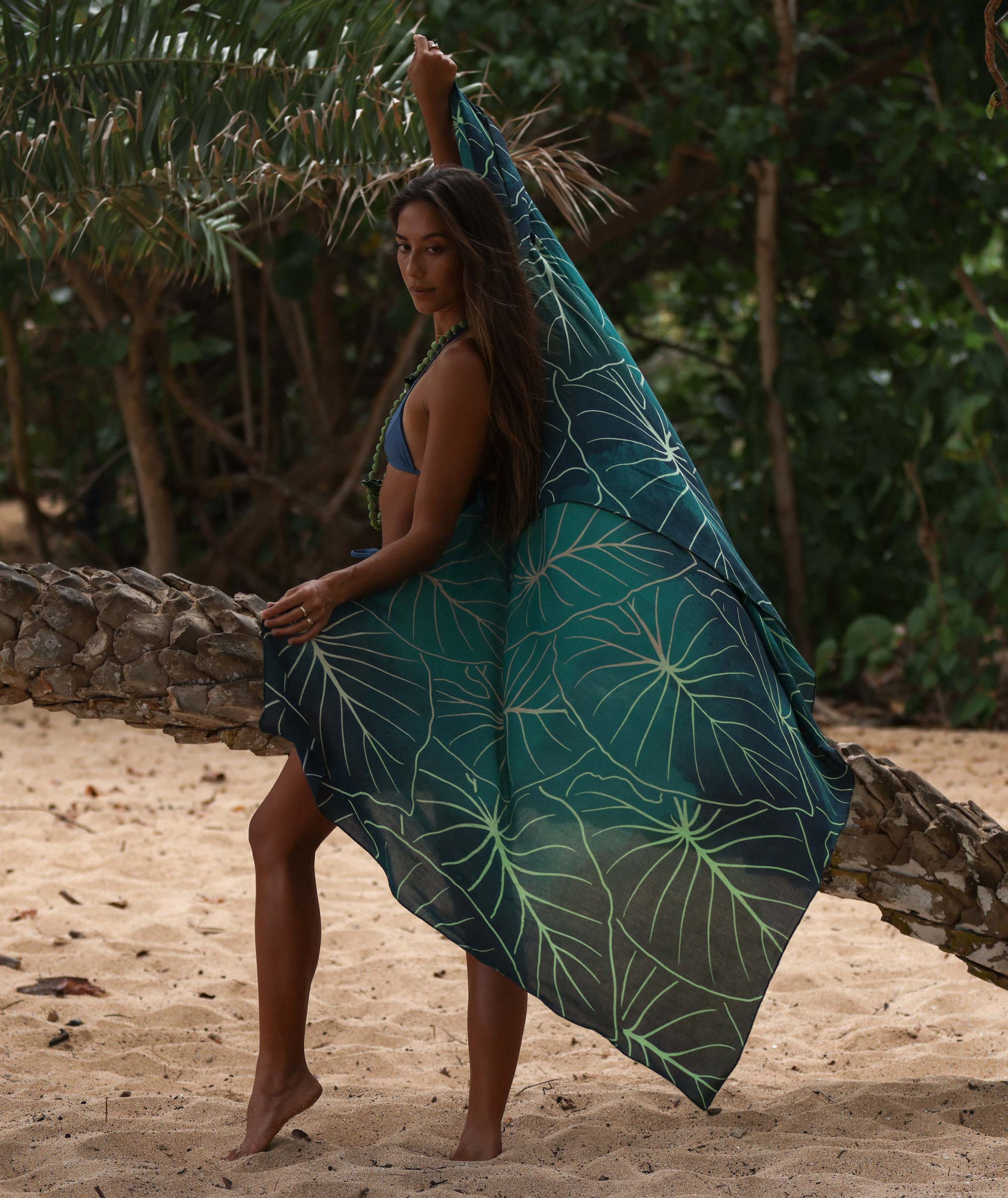 Woman holding a green leaf-patterned towel on a beach