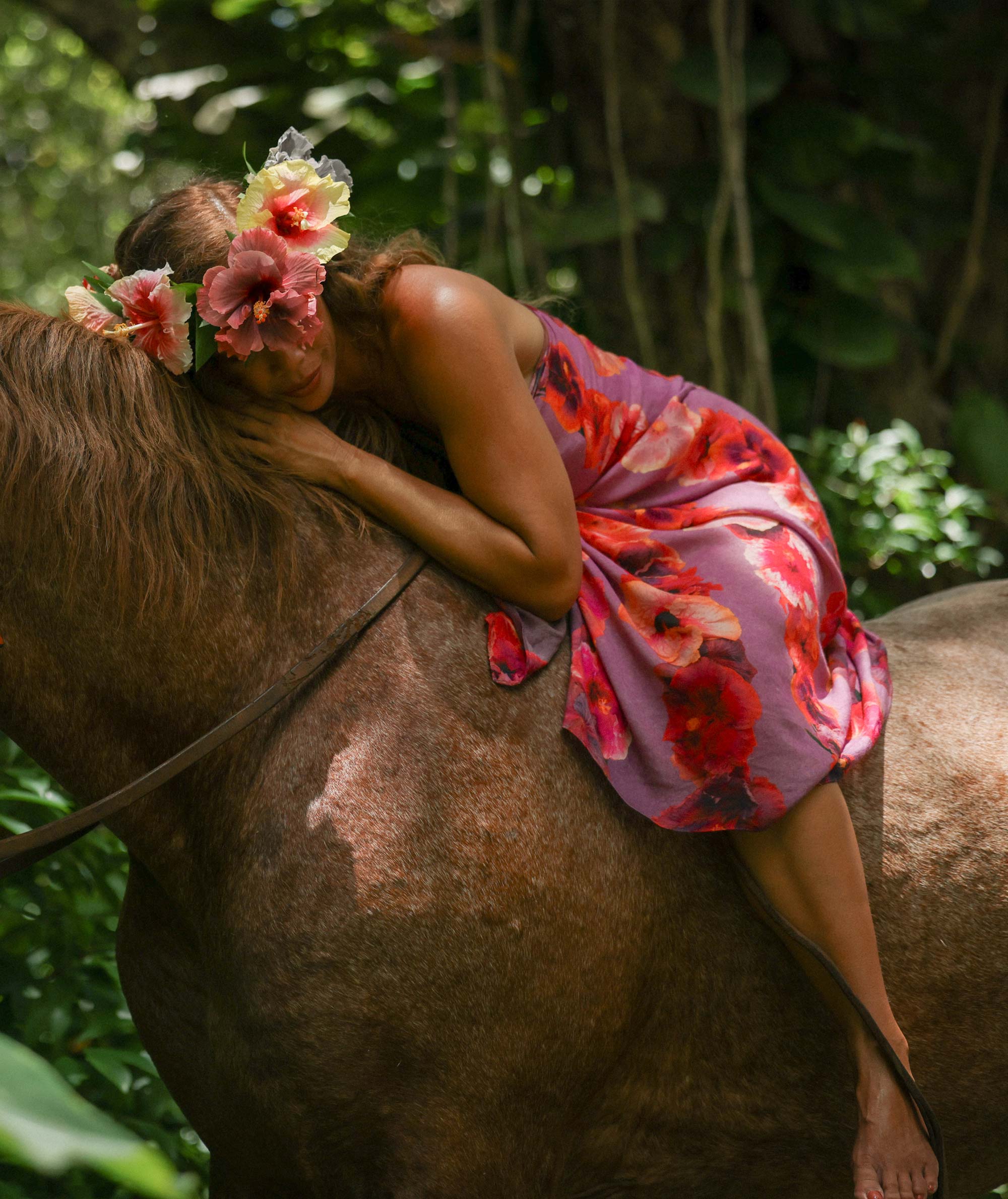 Person in a floral dress and headpiece sitting on a horse in a natural setting