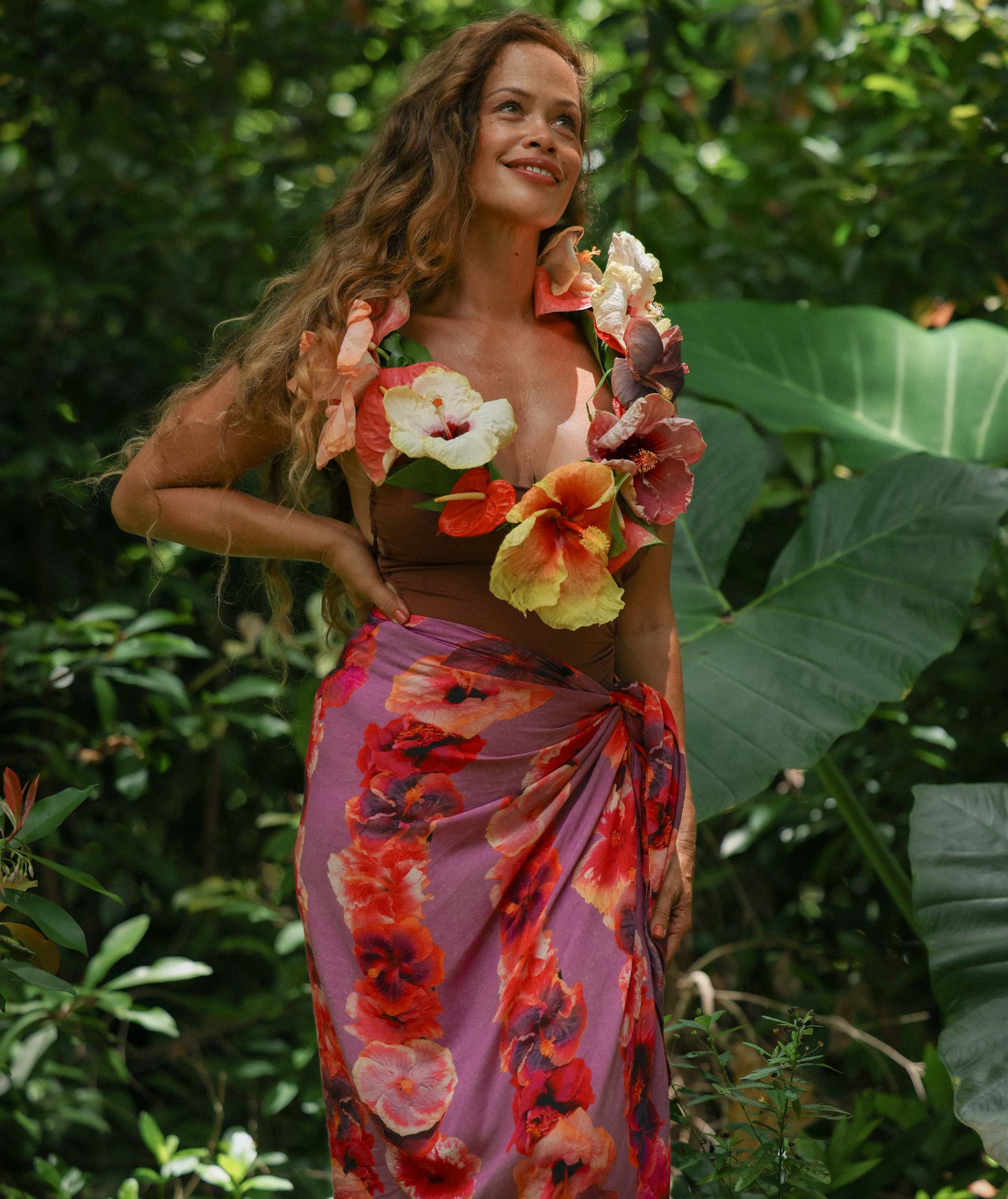 Woman in a colorful floral dress standing among green foliage