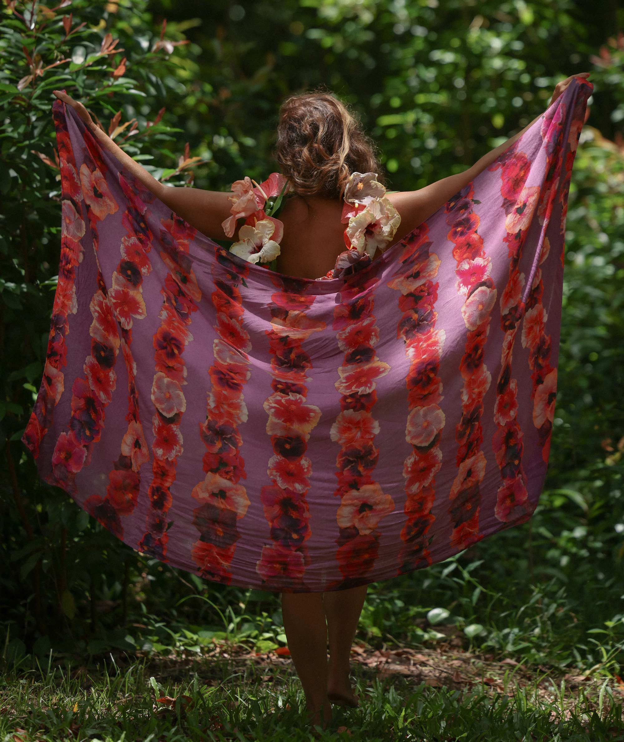 Person wearing a floral dress with a pattern of red and pink flowers in a garden setting