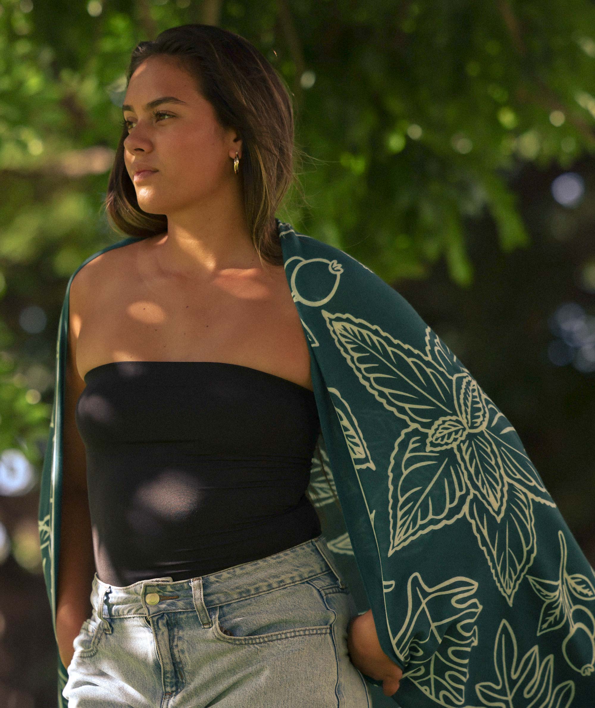 Woman holding a green towel with white patterns, standing outdoors with blurred greenery in the background