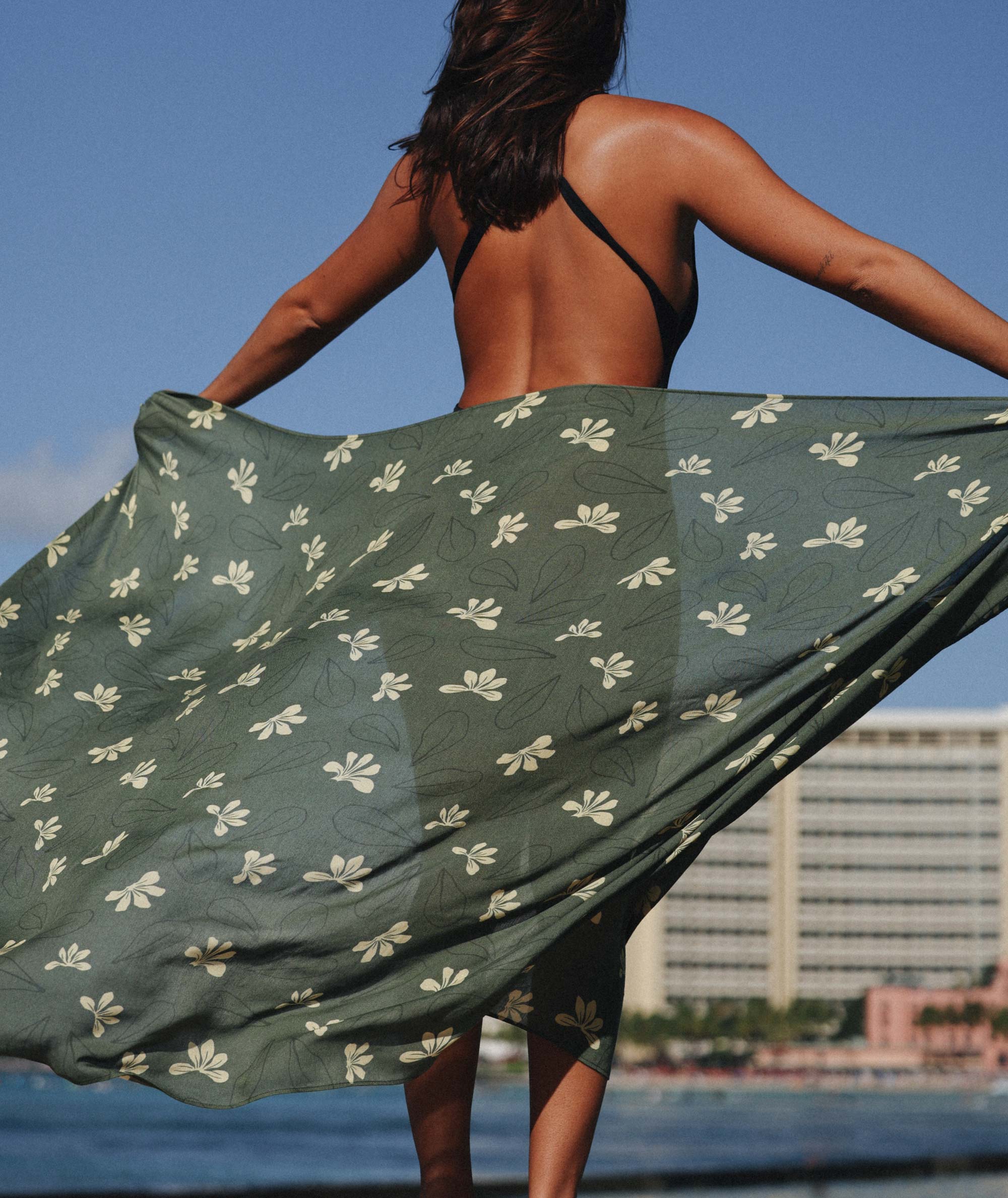 Person holding a green floral-patterned fabric with a cityscape in the background